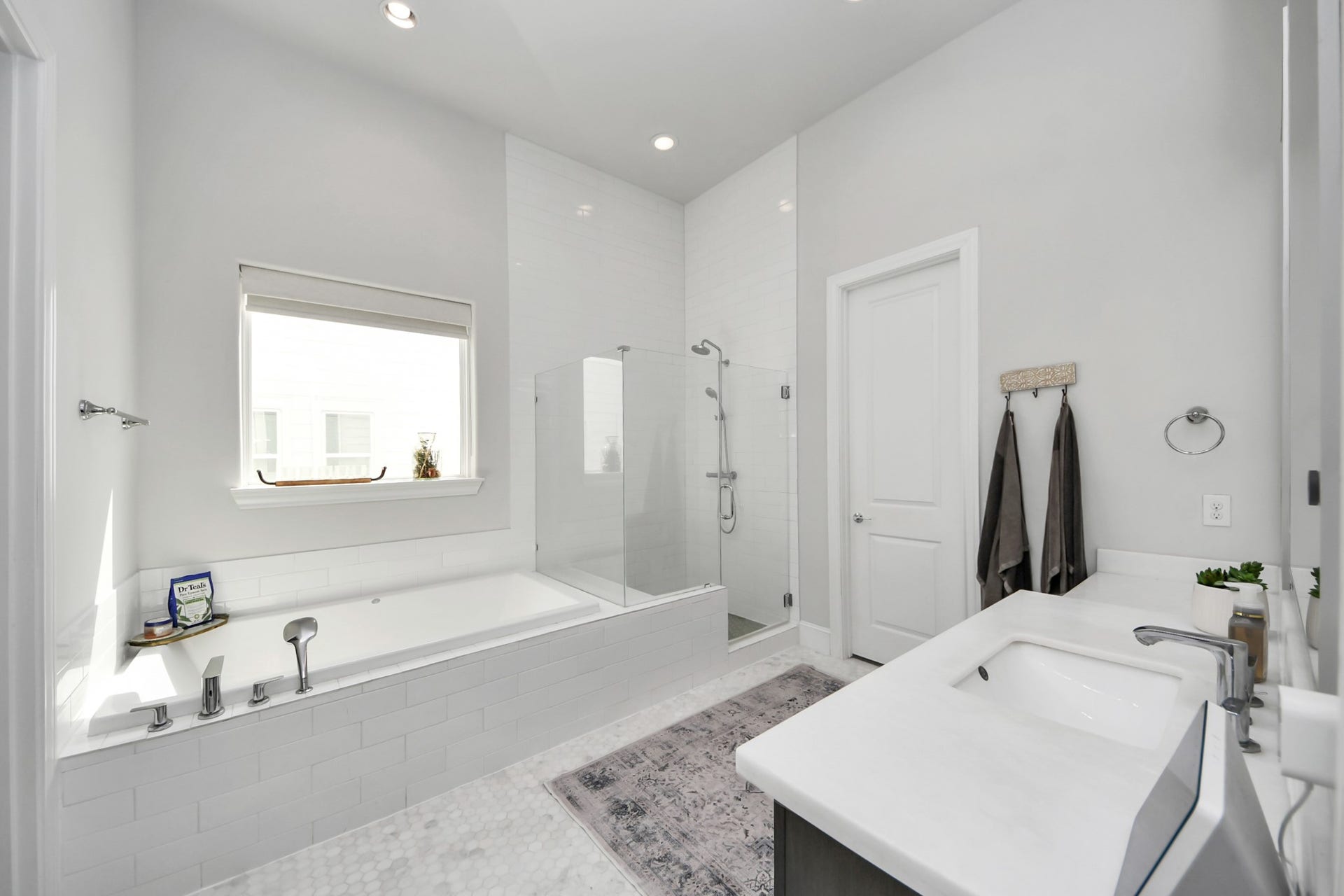 Elegant bathroom featuring a spacious soaking tub, glass-enclosed shower, and modern vanity with sleek fixtures, all bathed in natural light.