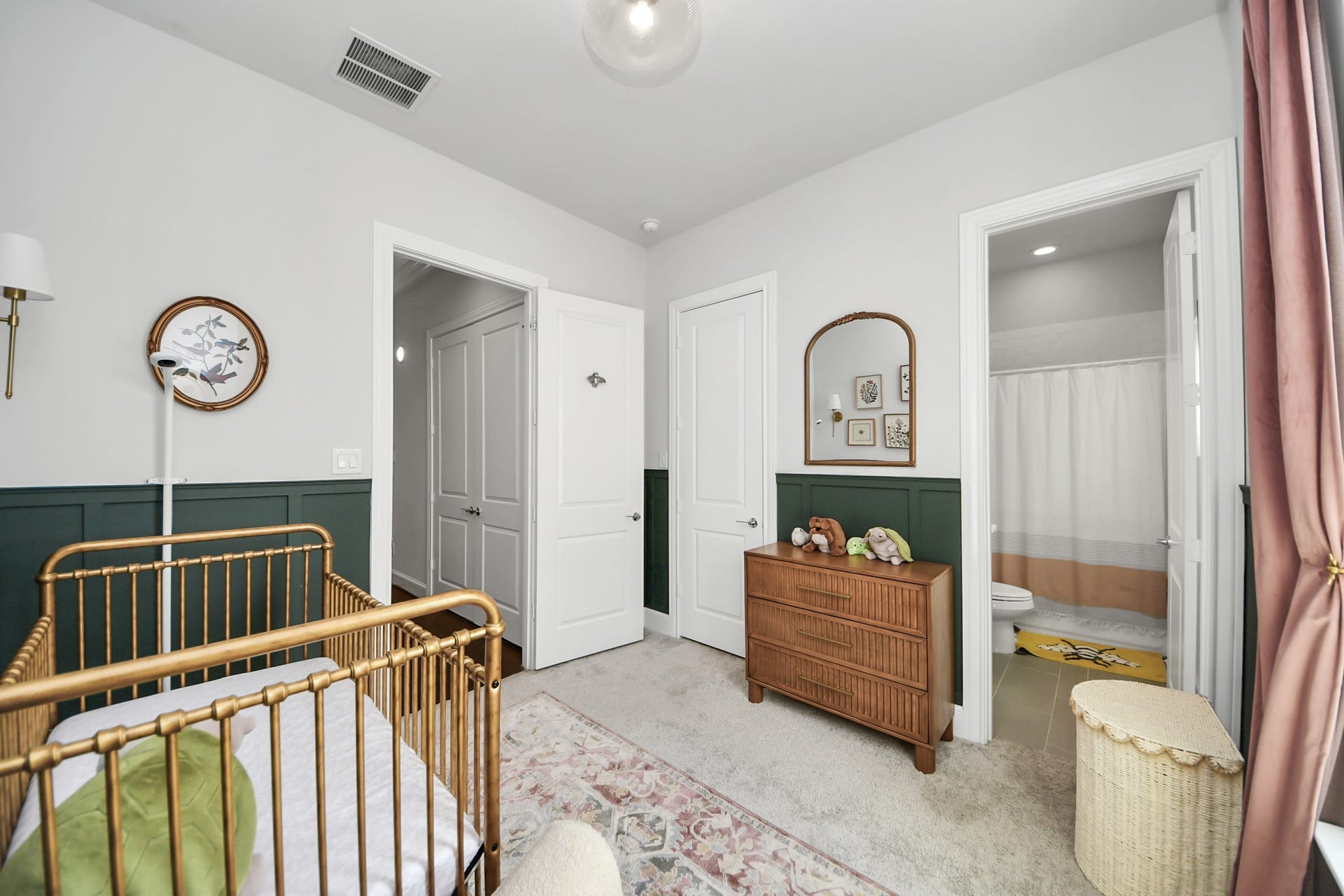 Charming nursery with a cozy crib, elegant wainscoting, and soft carpeting, featuring an en-suite bathroom for convenience.