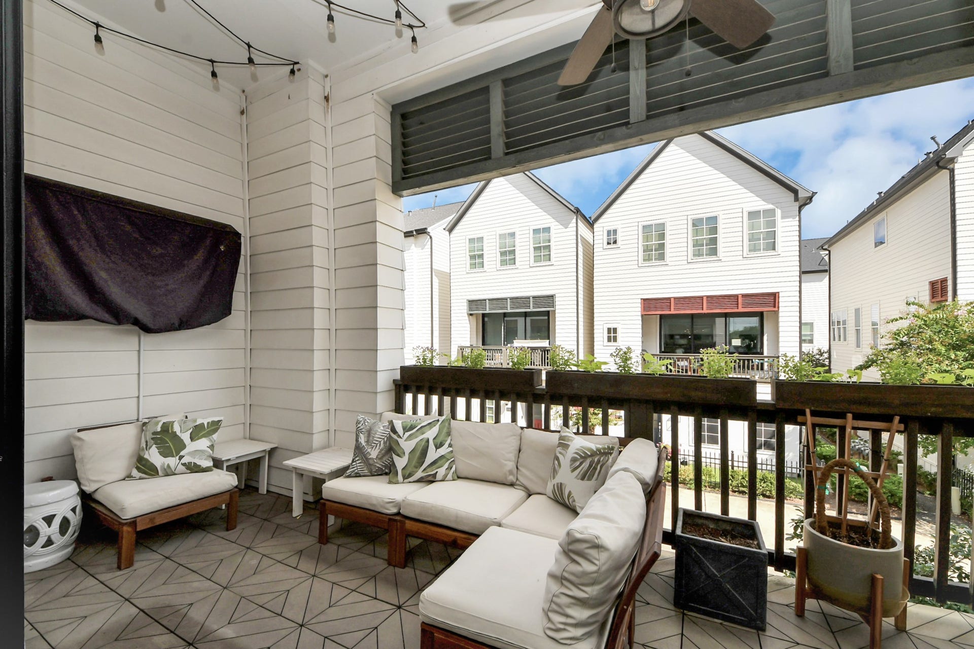 Charming covered patio featuring comfortable seating, stylish tile flooring, and a ceiling fan, perfect for relaxing and enjoying views of the neighboring homes.