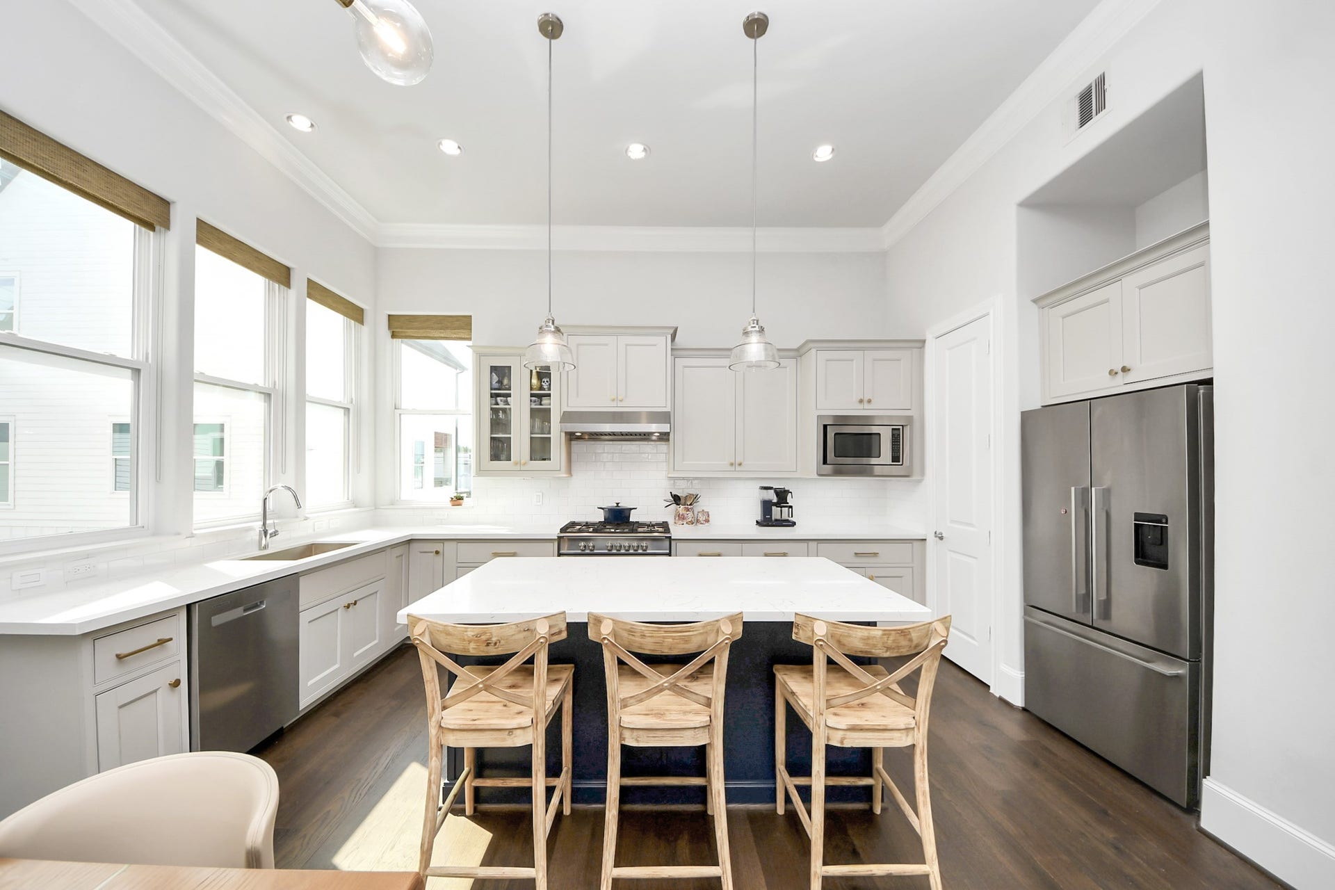 Bright and spacious kitchen featuring sleek white cabinetry, modern stainless steel appliances, and a large central island with seating, perfect for entertaining.