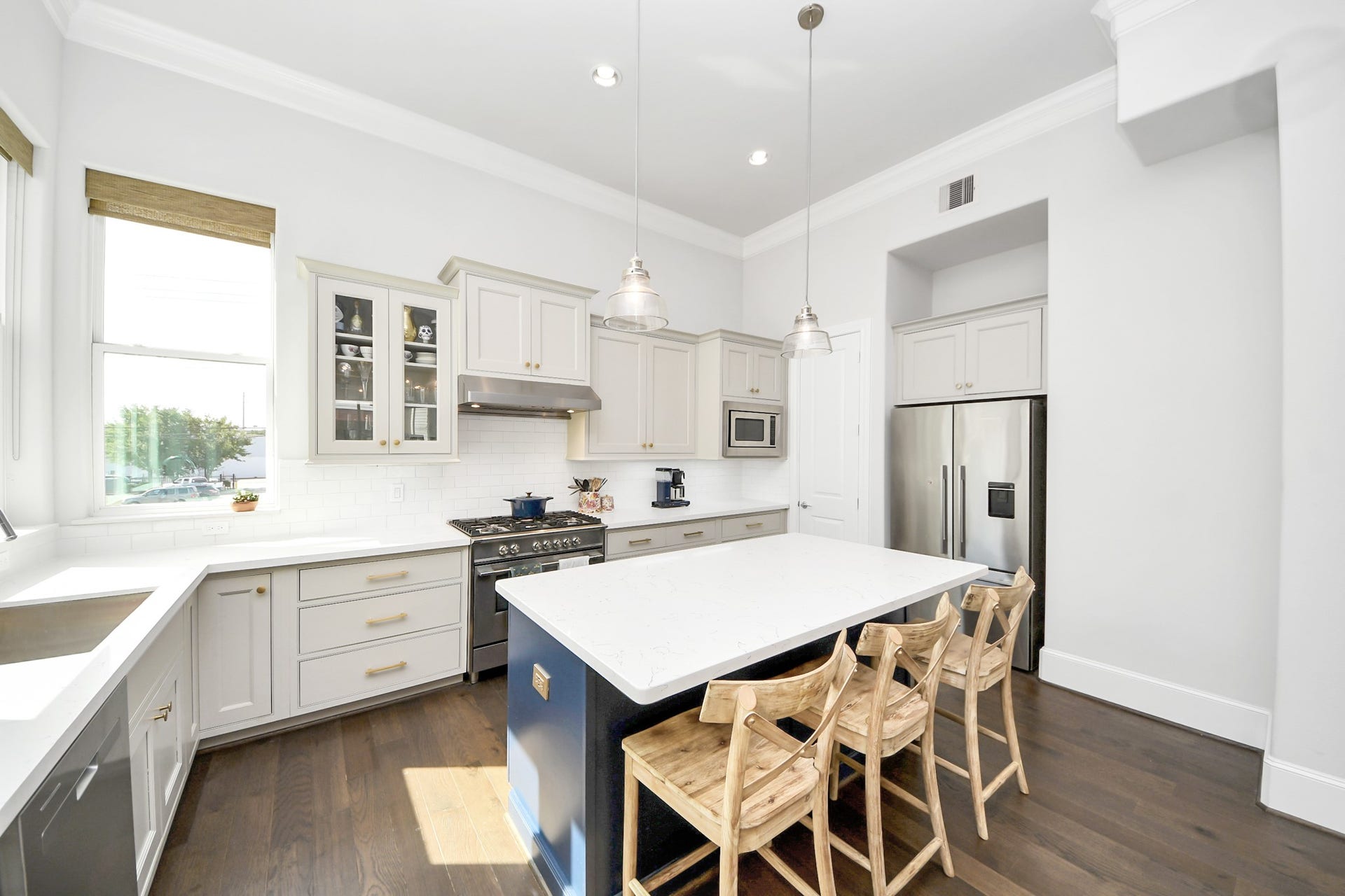 Bright and spacious modern kitchen featuring sleek white cabinetry, stainless steel appliances, an expansive island with seating, and abundant natural light from large windows.