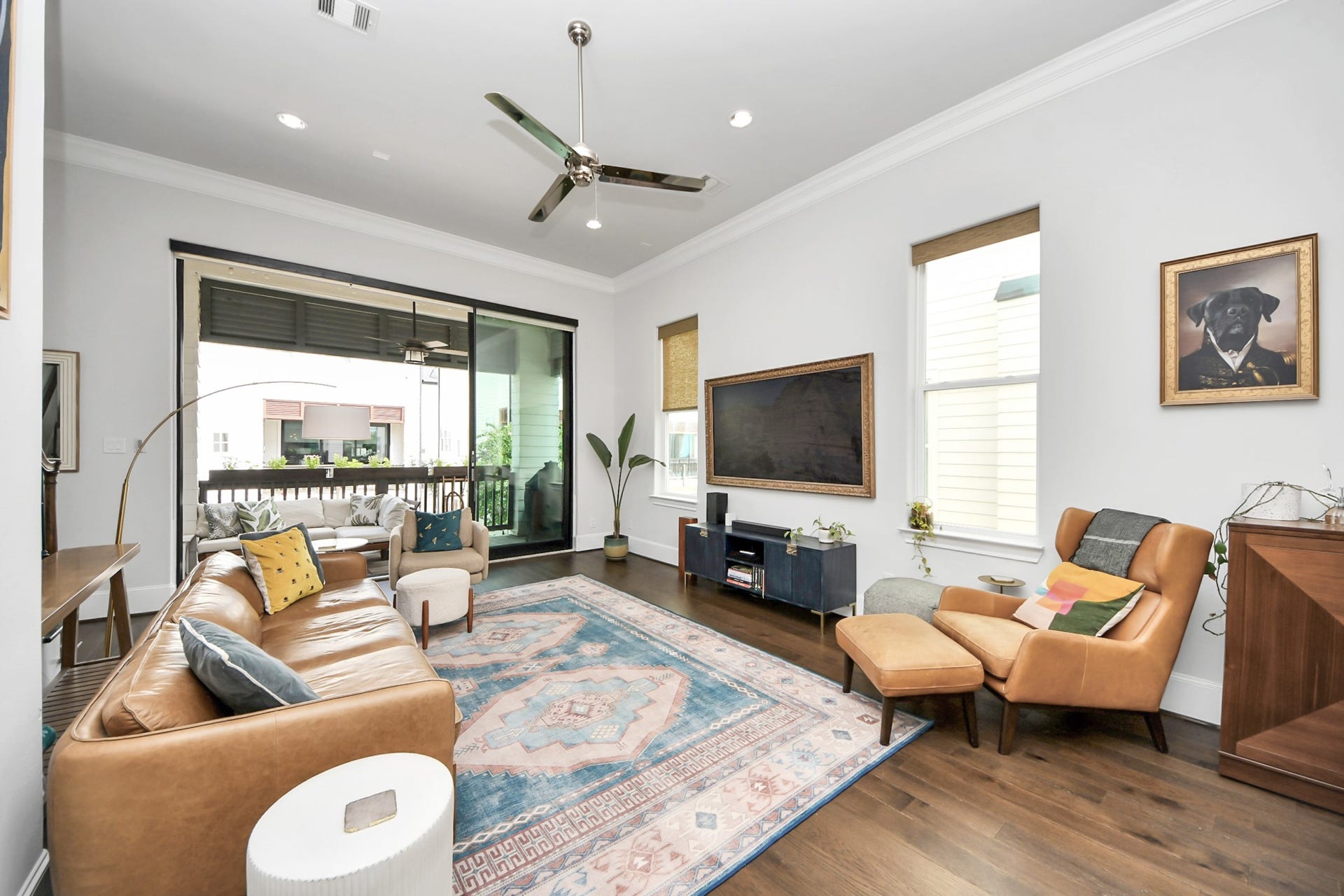 Bright and inviting living room featuring sleek hardwood floors, contemporary furniture, and a stylish ceiling fan, with large glass doors opening to a cozy balcony.