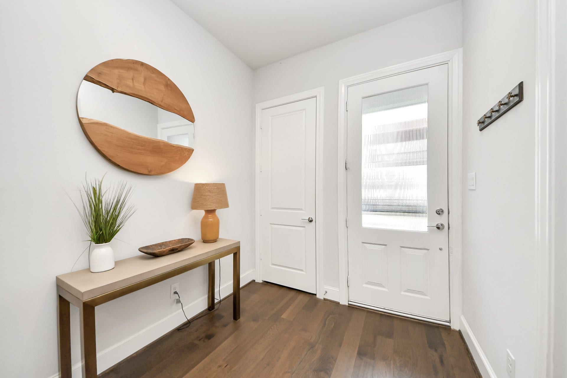 Inviting entryway featuring a stylish console table, modern decor, and a sleek round mirror, complemented by warm wood flooring.