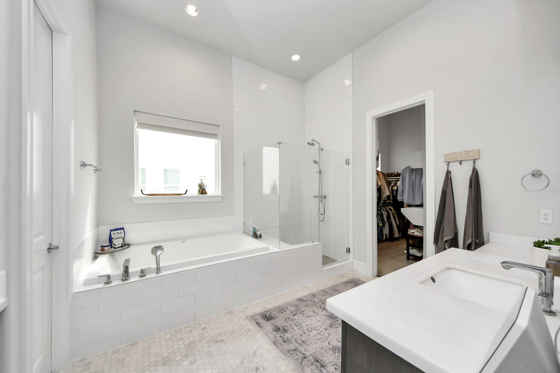 Spacious and modern bathroom featuring a large soaking tub, a glass-enclosed shower, and dual vanities with sleek fixtures, complemented by a walk-in closet.
