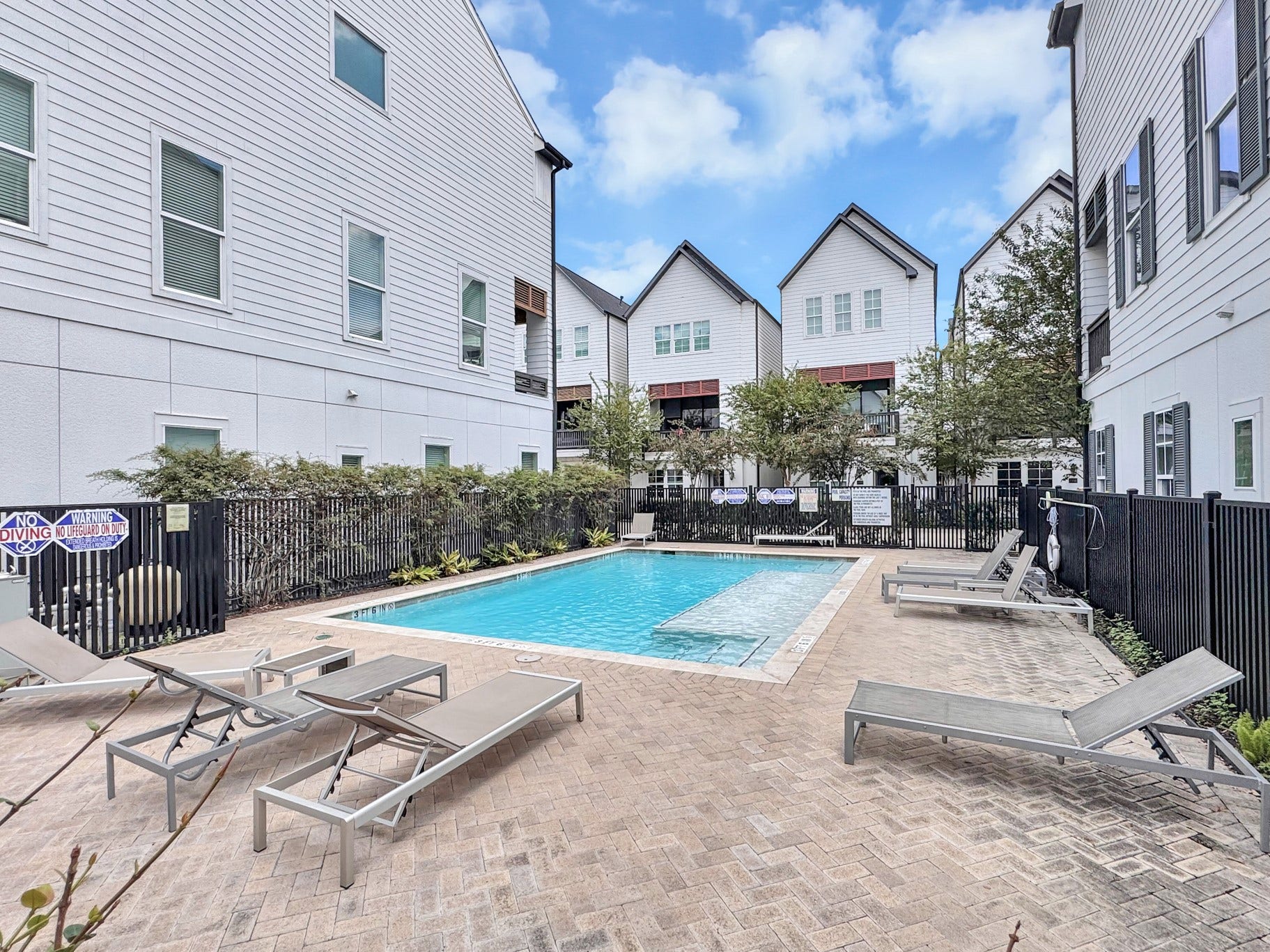 Charming community pool area surrounded by modern townhomes, featuring comfortable lounge chairs and a secure fence for privacy and relaxation.
