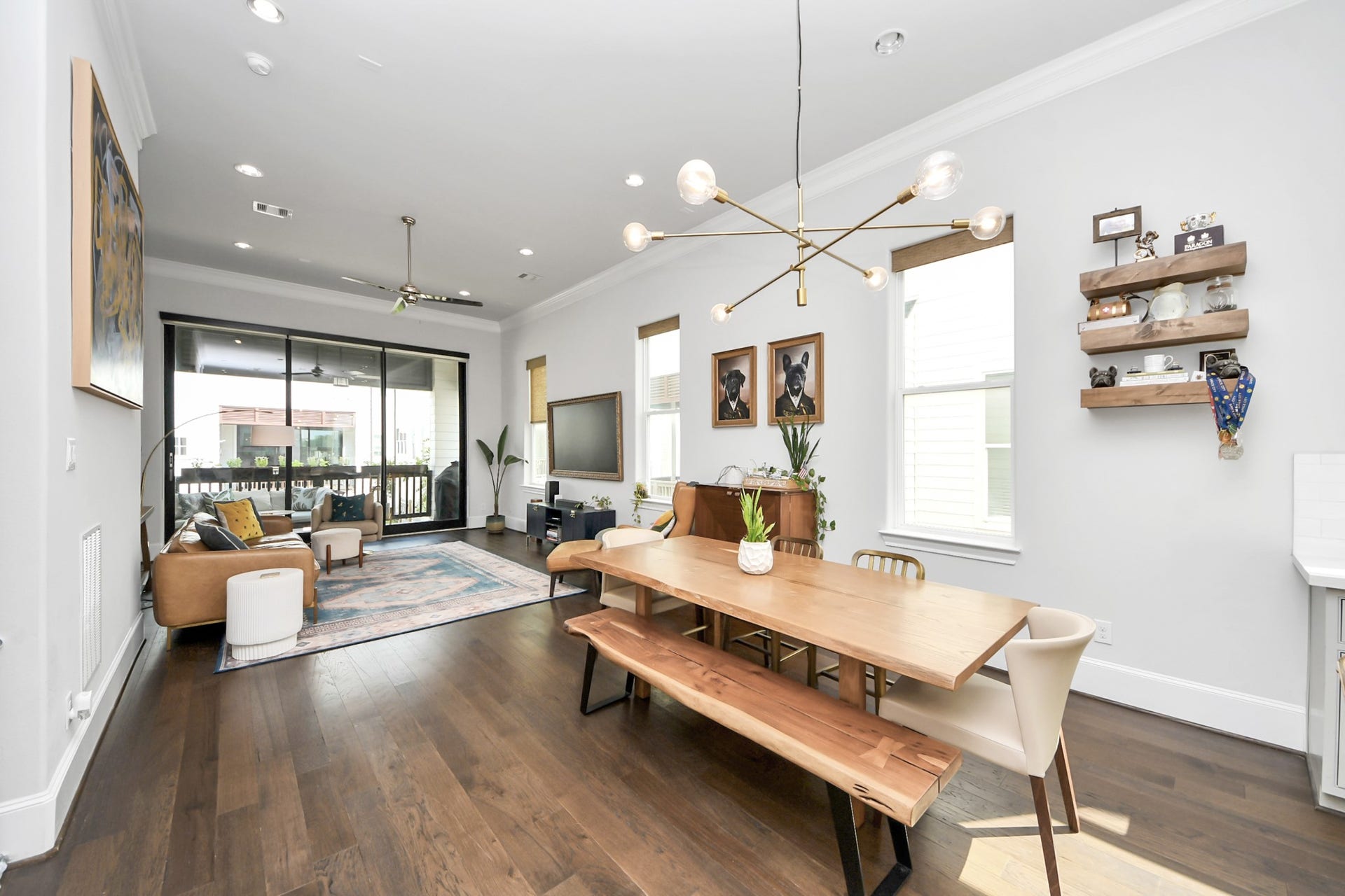 Spacious open-concept living and dining area features elegant hardwood floors, modern lighting, and large windows, leading to a cozy outdoor patio.