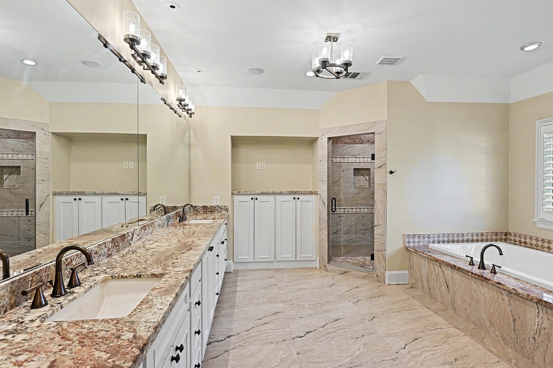 Luxrious primary bath offers a soaking garden tub, frameless glass-enclosed walk-in shower, dual sinks, generous countertop space, and built-in storage.