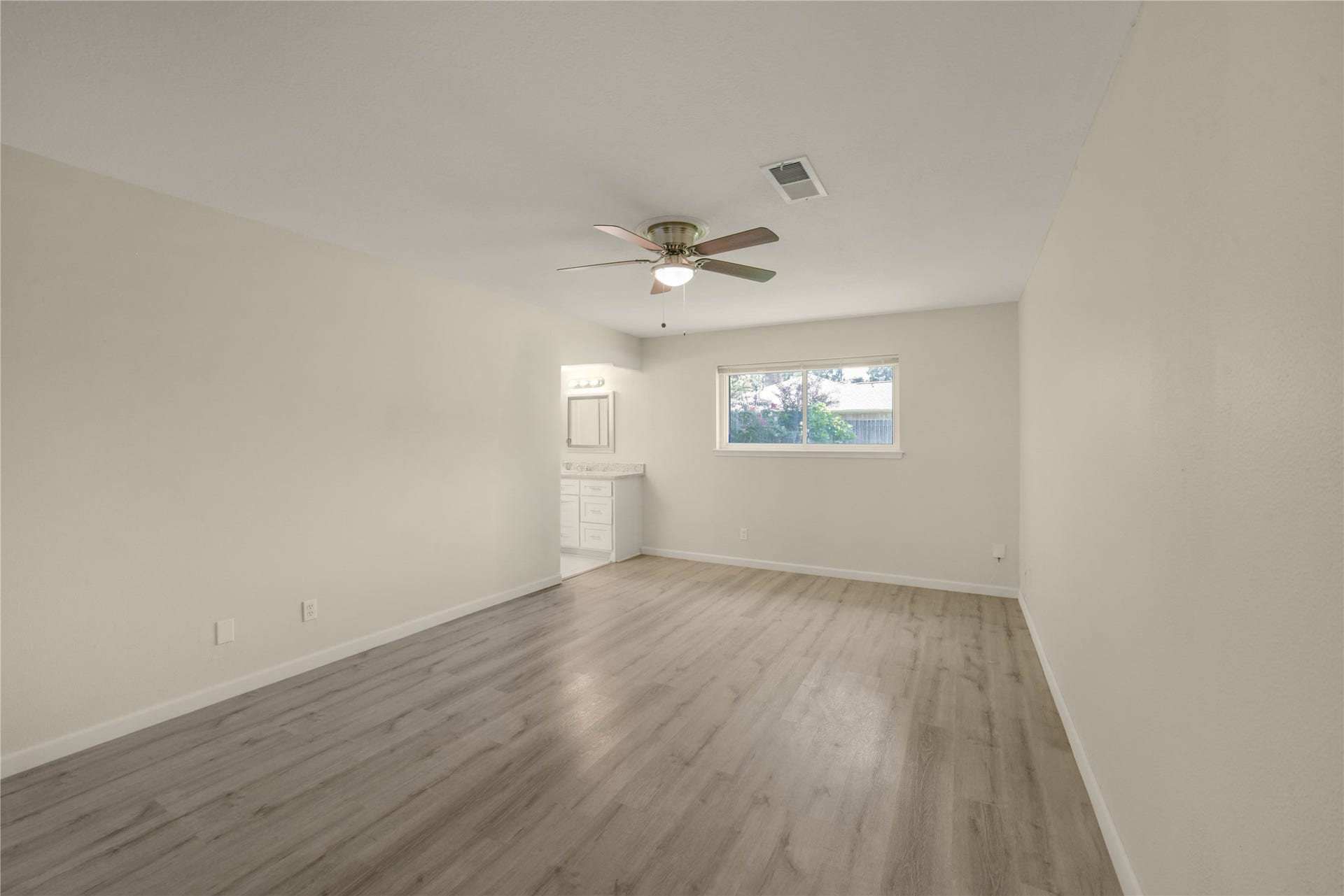 Spacious primary bedroom featuring a ceiling fan, fresh neutral paint, and a large window with backyard views. A convenient ensuite bathroom with vanity and mirror completes this comfortable, private retreat.