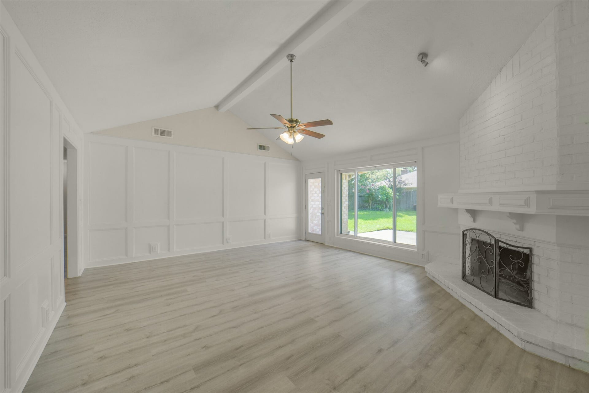 Open living room featuring a vaulted ceiling with ceiling fan, a fireplace, wood-look flooring, and fresh neutral paint throughout. This is a spacious, light-filled living room ideal for entertaining.