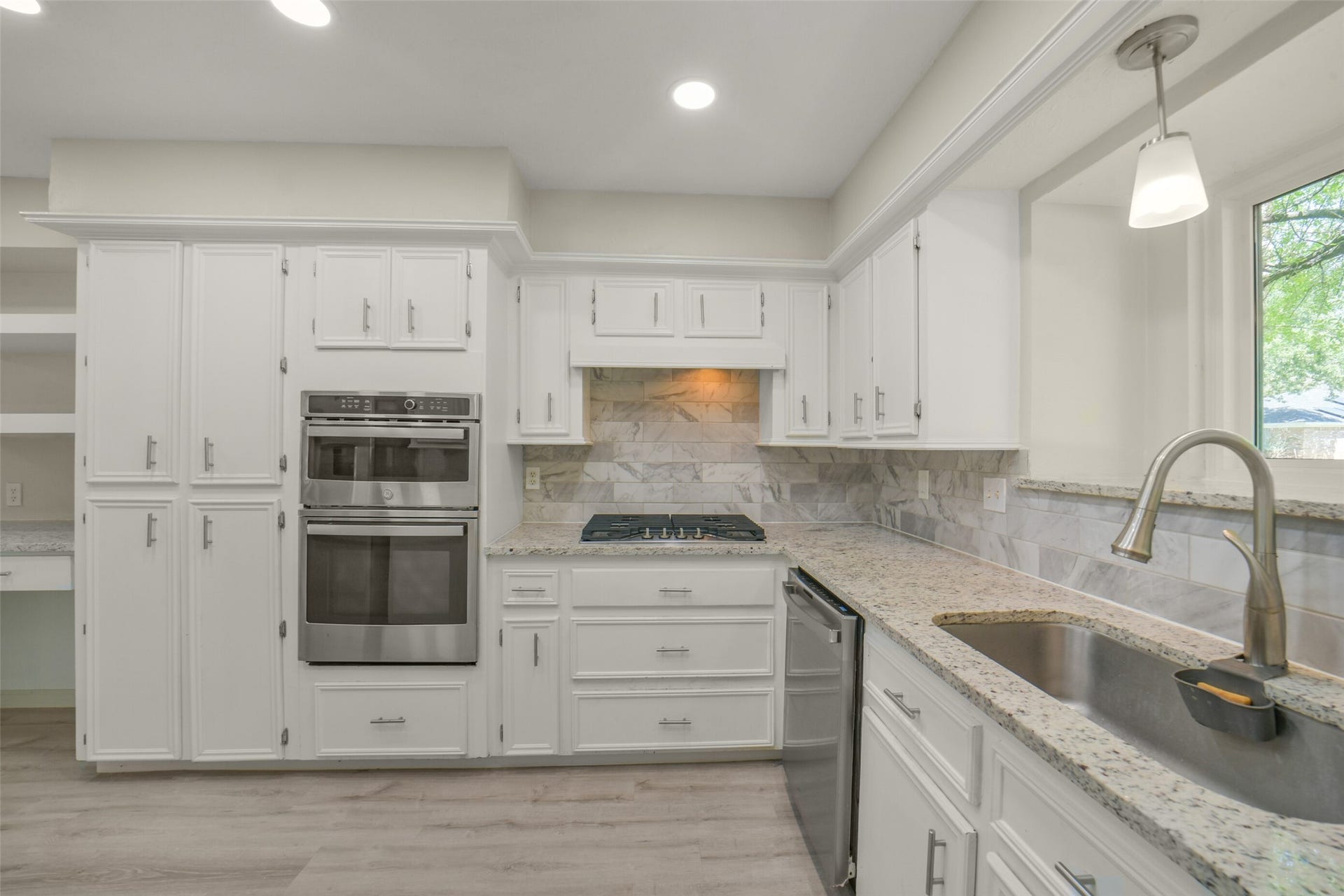 Beautifully updated kitchen featuring crisp white cabinetry, granite countertops, and a full stainless steel appliance package including a double wall oven, gas cooktop, and dishwasher. A stylish marble-look tile backsplash, ample storage, and a large sink with gooseneck faucet complete this functional and elegant space.