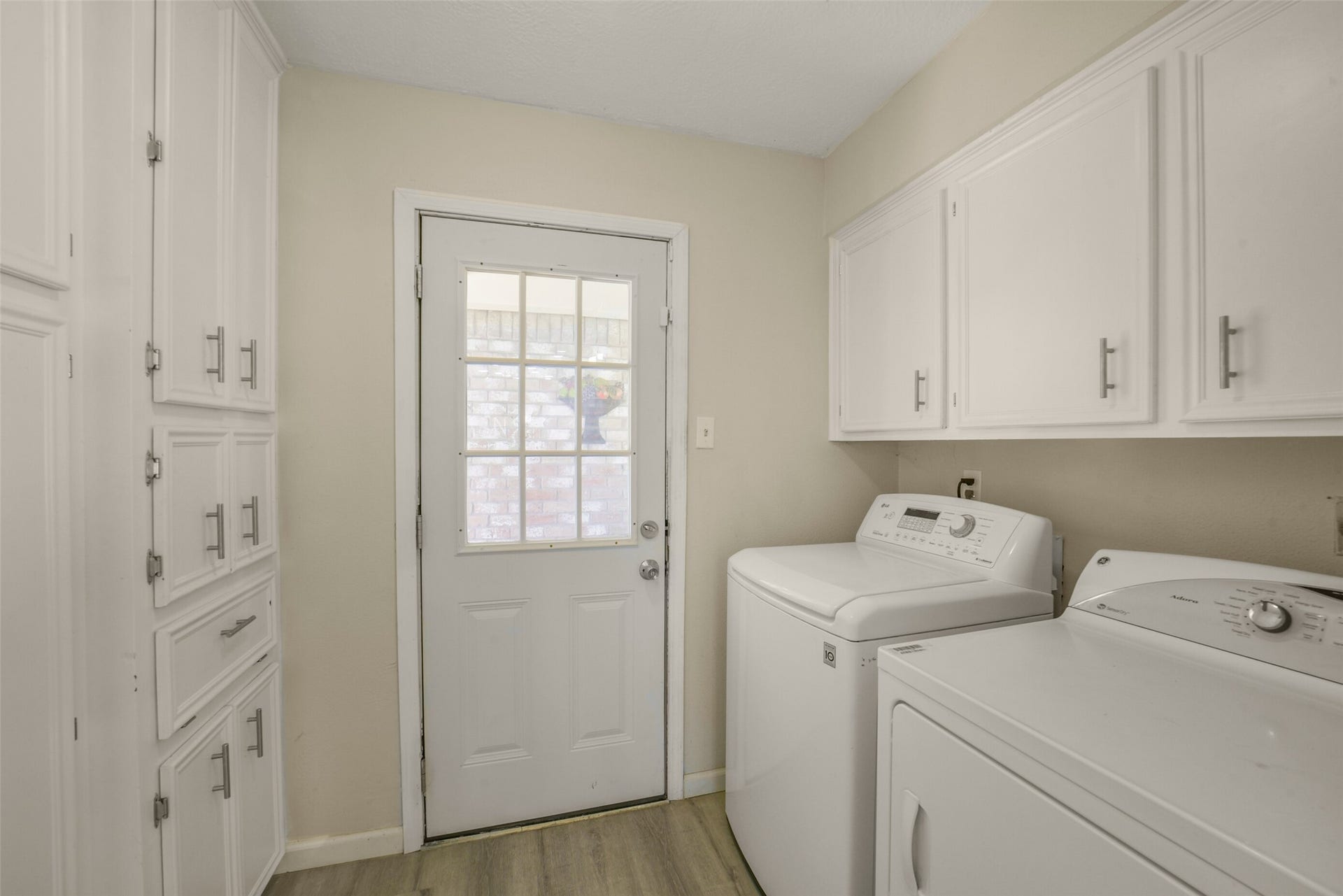 Convenient laundry room featuring plenty of white cabinet storage, a side door leading outside, and space for full-size washer and dryer  a practical, well-organized area for everyday household tasks.