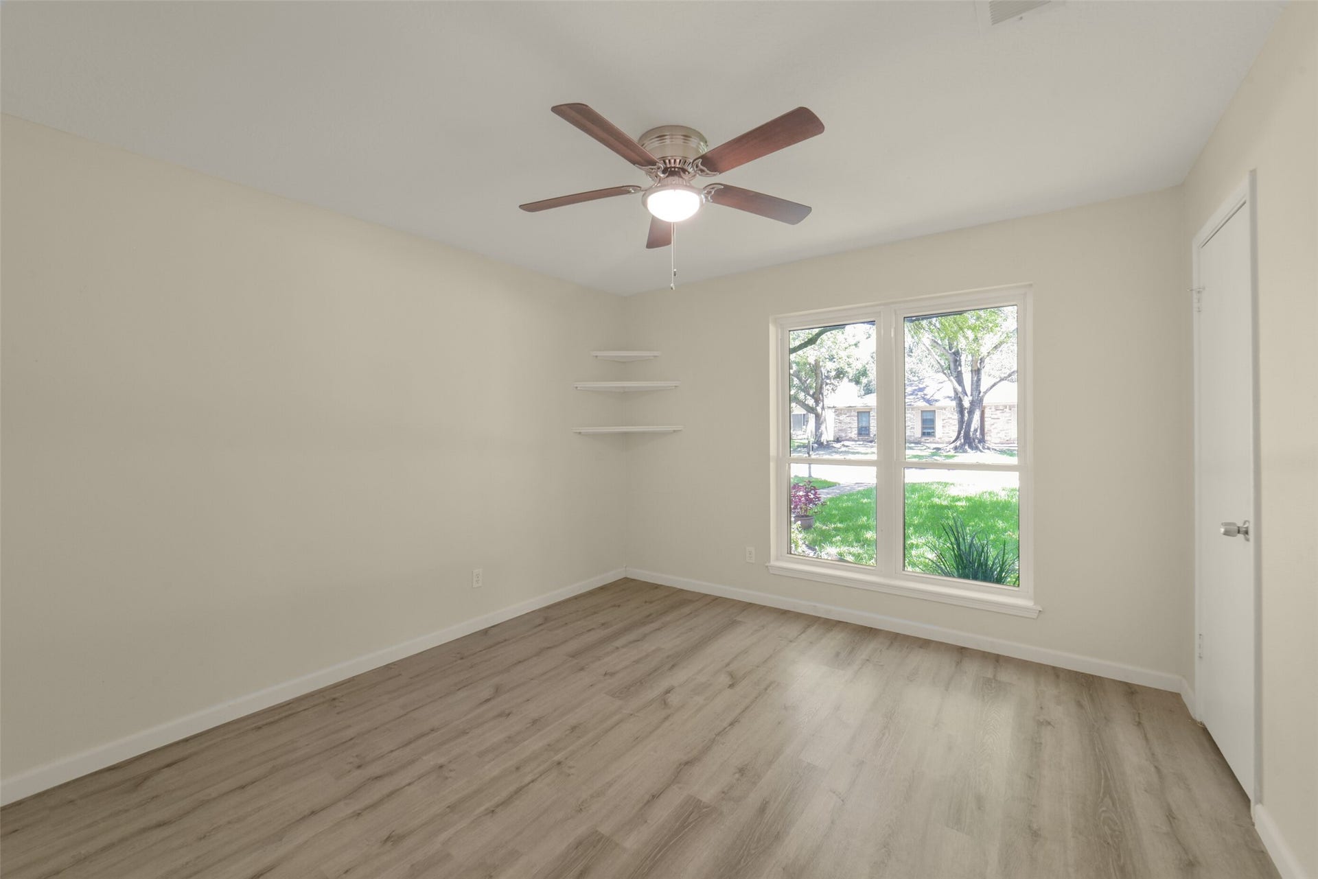 Rare third secondary bedroom offering a large window with charming street views, a ceiling fan, fresh neutral paint, corner shelving, and a closet  a comfortable, light-filled space.