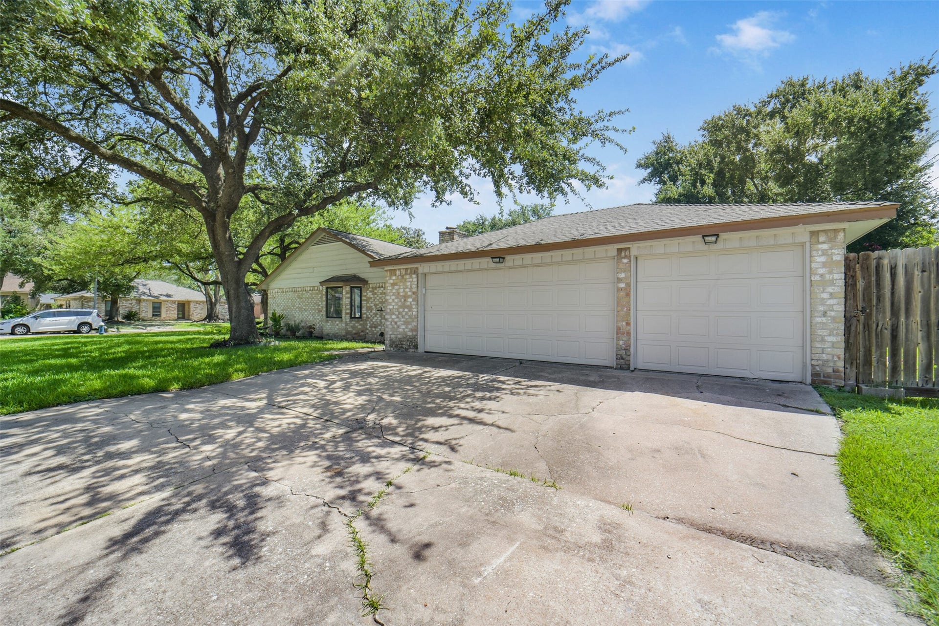 Rare find for the neighborhood  this home offers a spacious three-car garage with a wide concrete driveway, all set beneath mature shade trees on a well-maintained brick exterior.