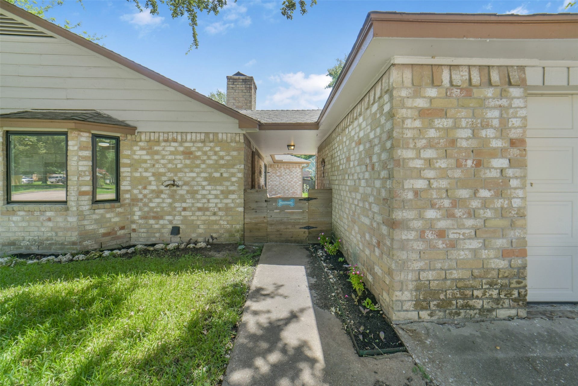Side view of the brick home showing the covered breezeway entrance with a charming gated walkway, mature landscaping, and easy access between the front and side yards  adding both curb appeal and functional flow to the property.