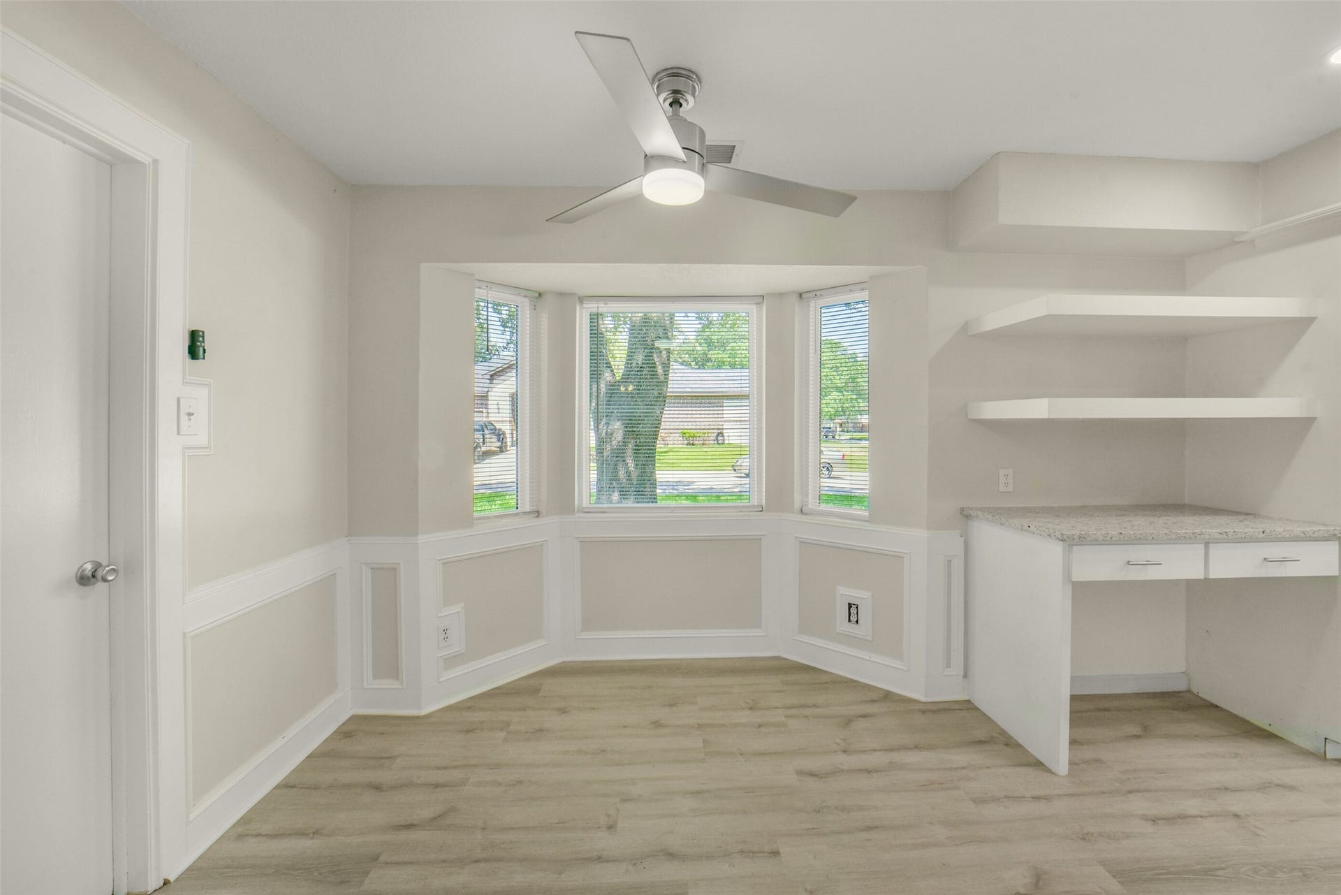 Lovely breakfast nook framed by a bright bay window overlooking the front lawn, with elegant wainscoting, a built-in granite-topped desk with storage drawers, and open shelving. This space offers a stylish, functional space for casual dining as well as a home office nook.