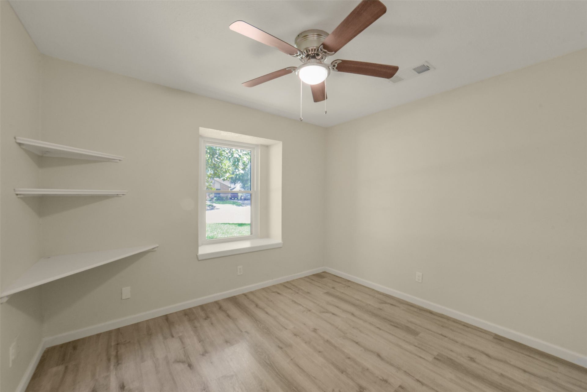 Bright 2nd secondary bedroom featuring a ceiling fan, fresh neutral paint, a large window with peaceful views, and built-in corner shelving  a versatile space perfect for a bedroom, home office, or study.