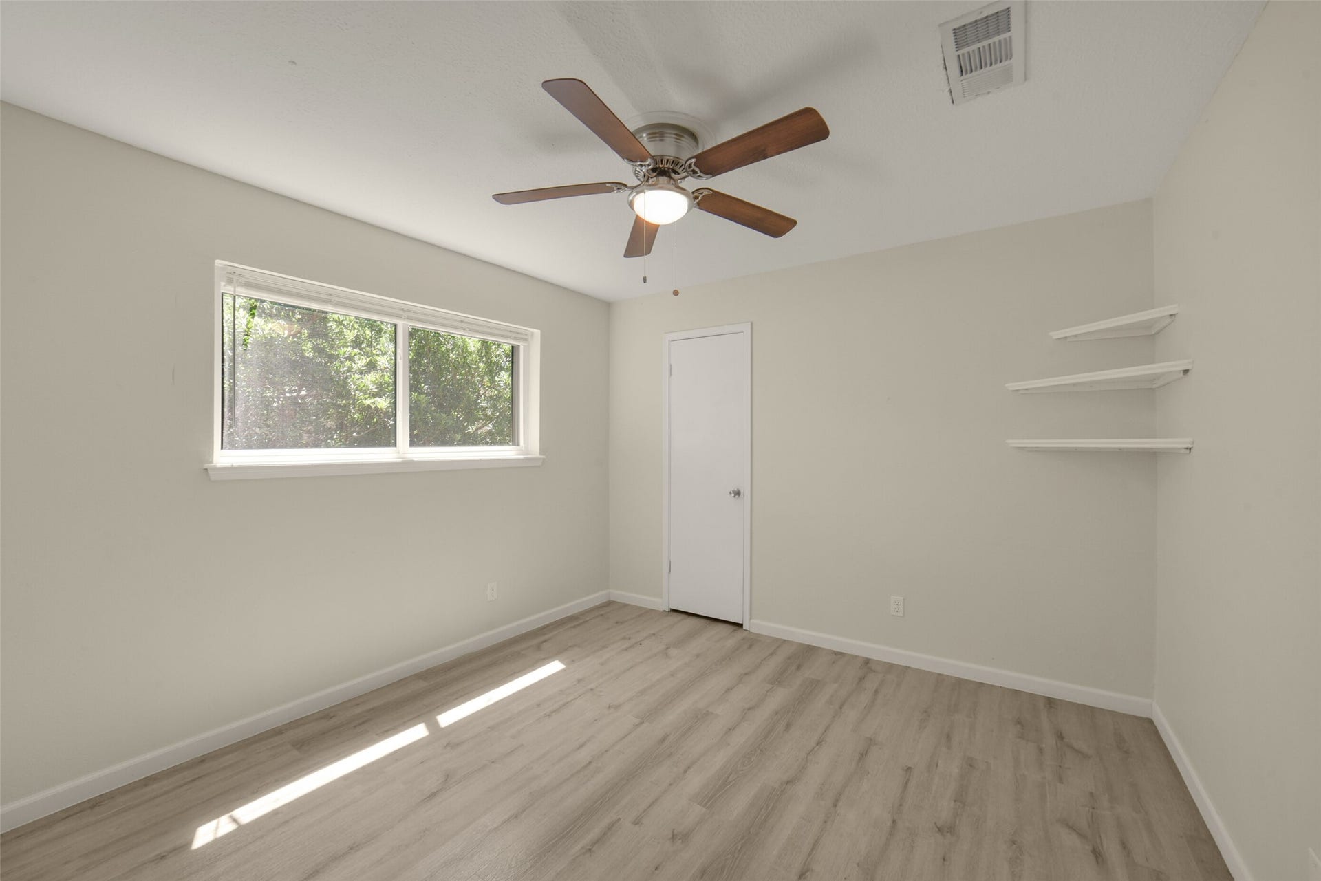 First spacious secondary bedroom featuring a ceiling fan, fresh neutral paint, a closet, and built-in corner shelving, plus a large window overlooking mature trees for lovely natural light and privacy.