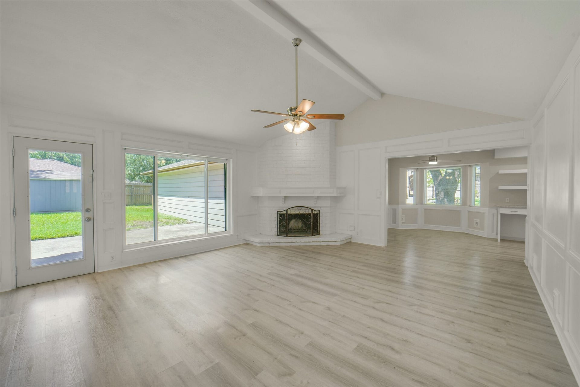 Large windows and a glass-paned door flood the space with natural light and offer backyard views, while the open layout flows seamlessly into an adjoining bay-windowed sitting area.