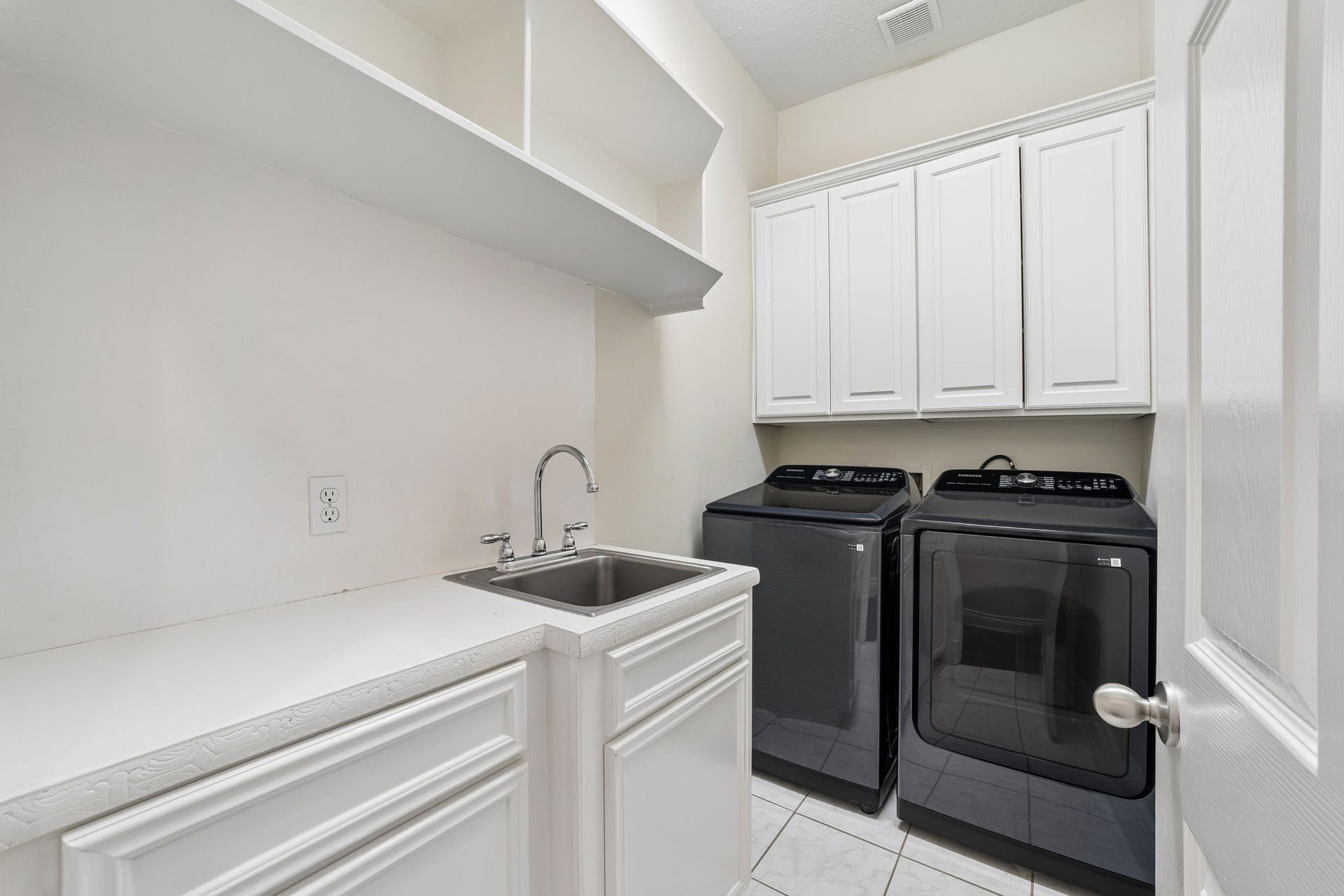 Spacious laundry room with sleek black appliances (not included in the sale, negotialble), ample white cabinetry for storage, and a convenient utility sink.