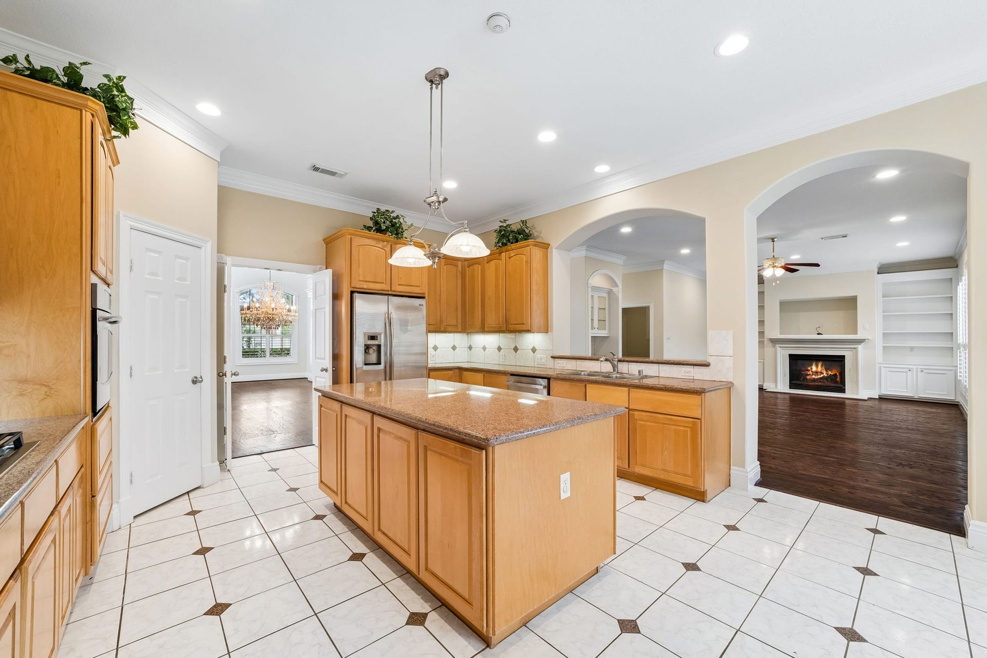 Spacious kitchen featuring warm wood cabinetry, sleek stainless steel appliances, and a central island, all under elegant recessed lighting.