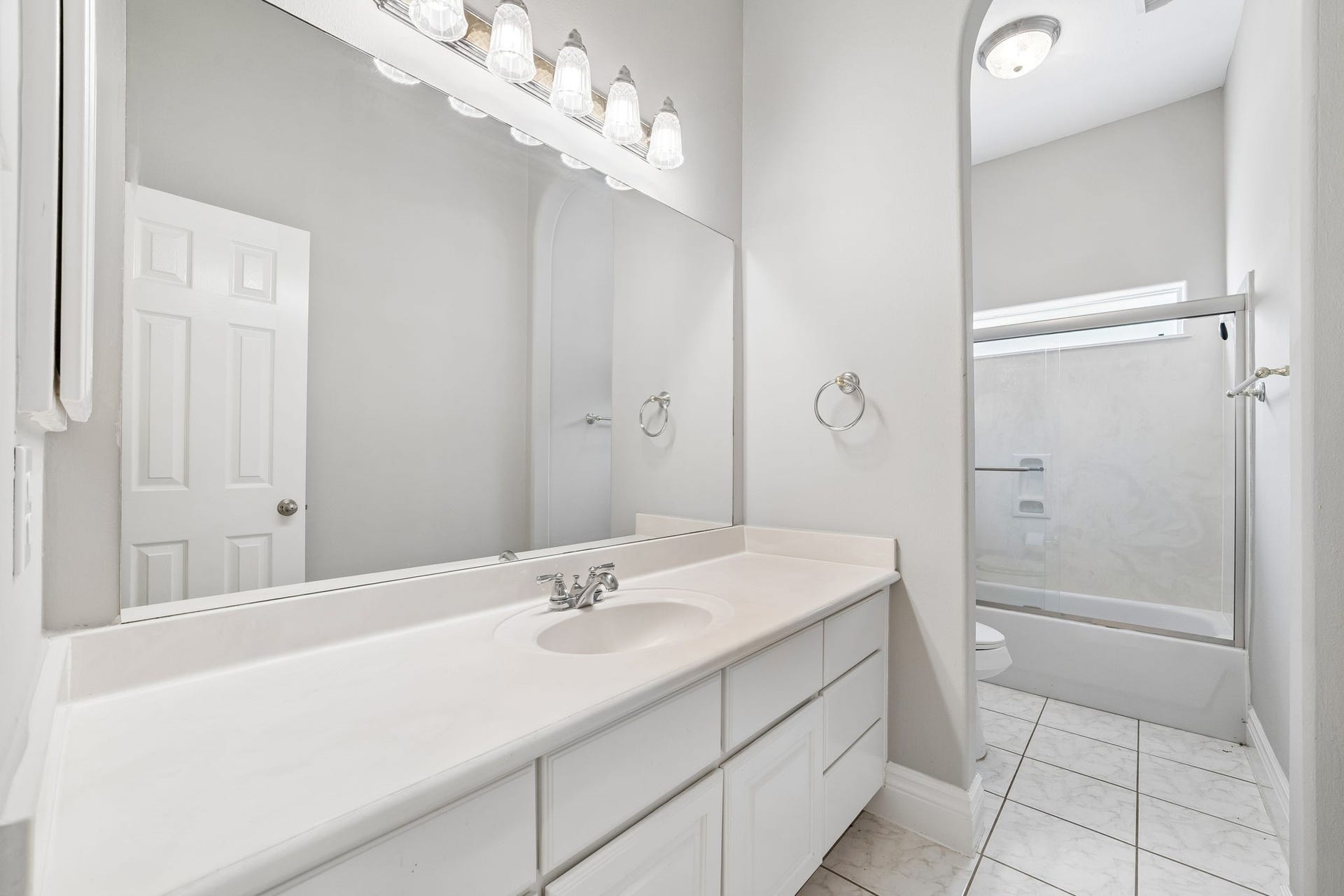 Bright and spacious bathroom in the first floor, featuring a large mirror, sleek vanity with ample storage, and a modern shower-tub combination.