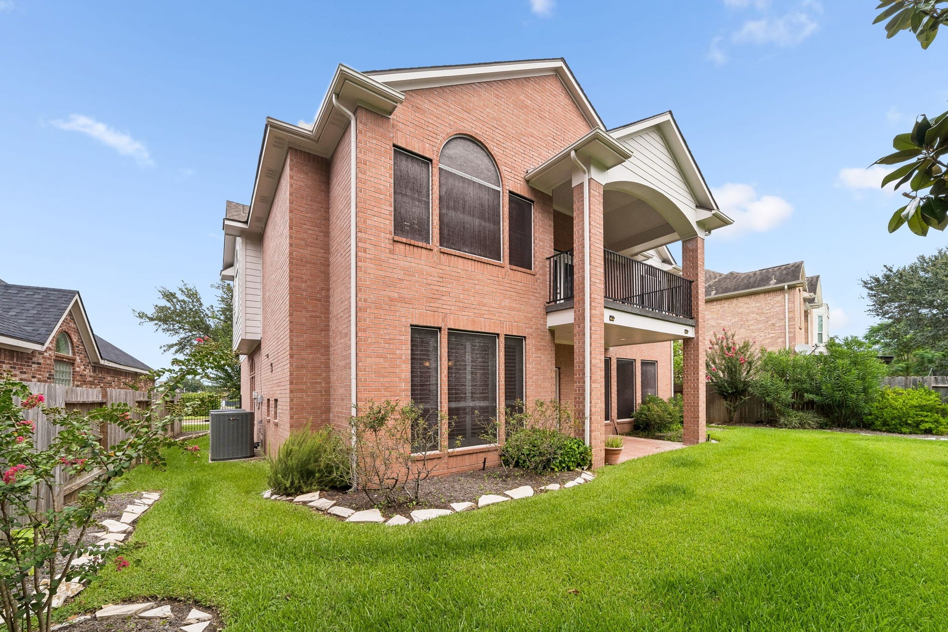 Elegant two-story brick home featuring a spacious balcony and covered patio, surrounded by a lush, well-manicured lawn.