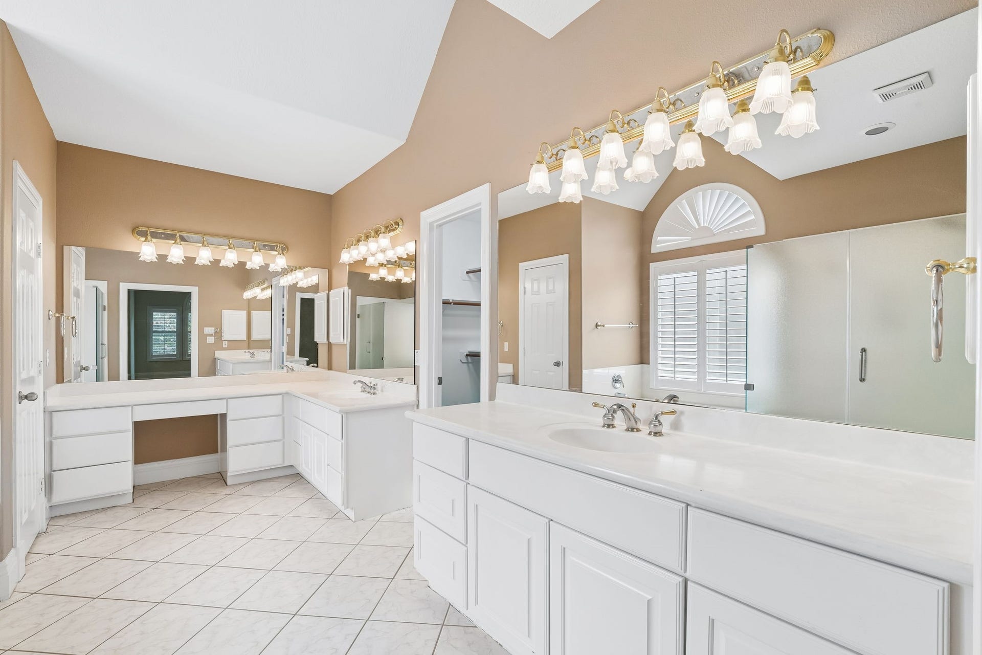 Spacious bathroom featuring dual vanities, abundant lighting, a luxurious soaking tub, and a sleek glass-enclosed shower.