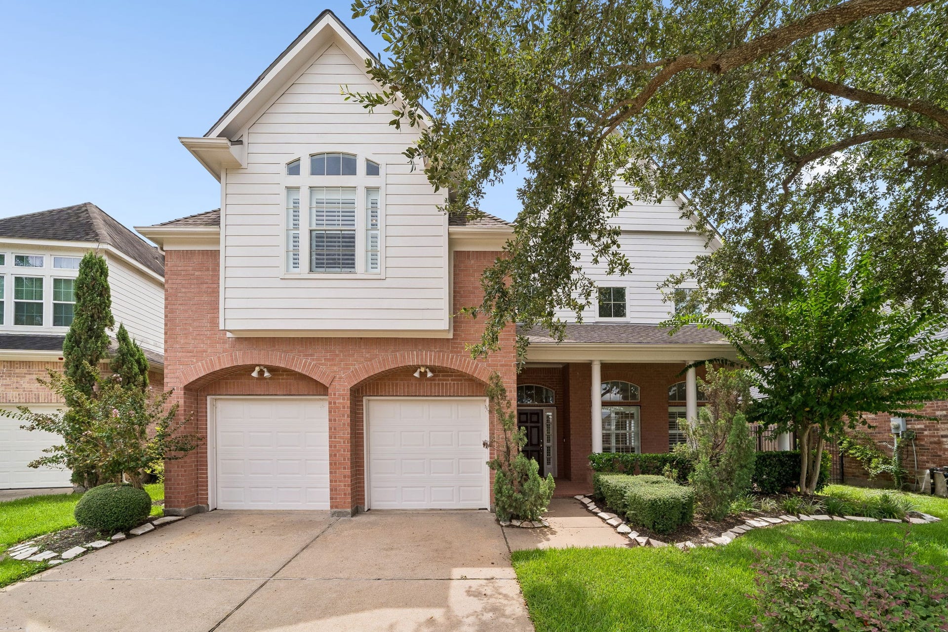 Charming two-story home with a welcoming brick facade, elegant arched windows, and a double garage, nestled in a beautifully landscaped setting.