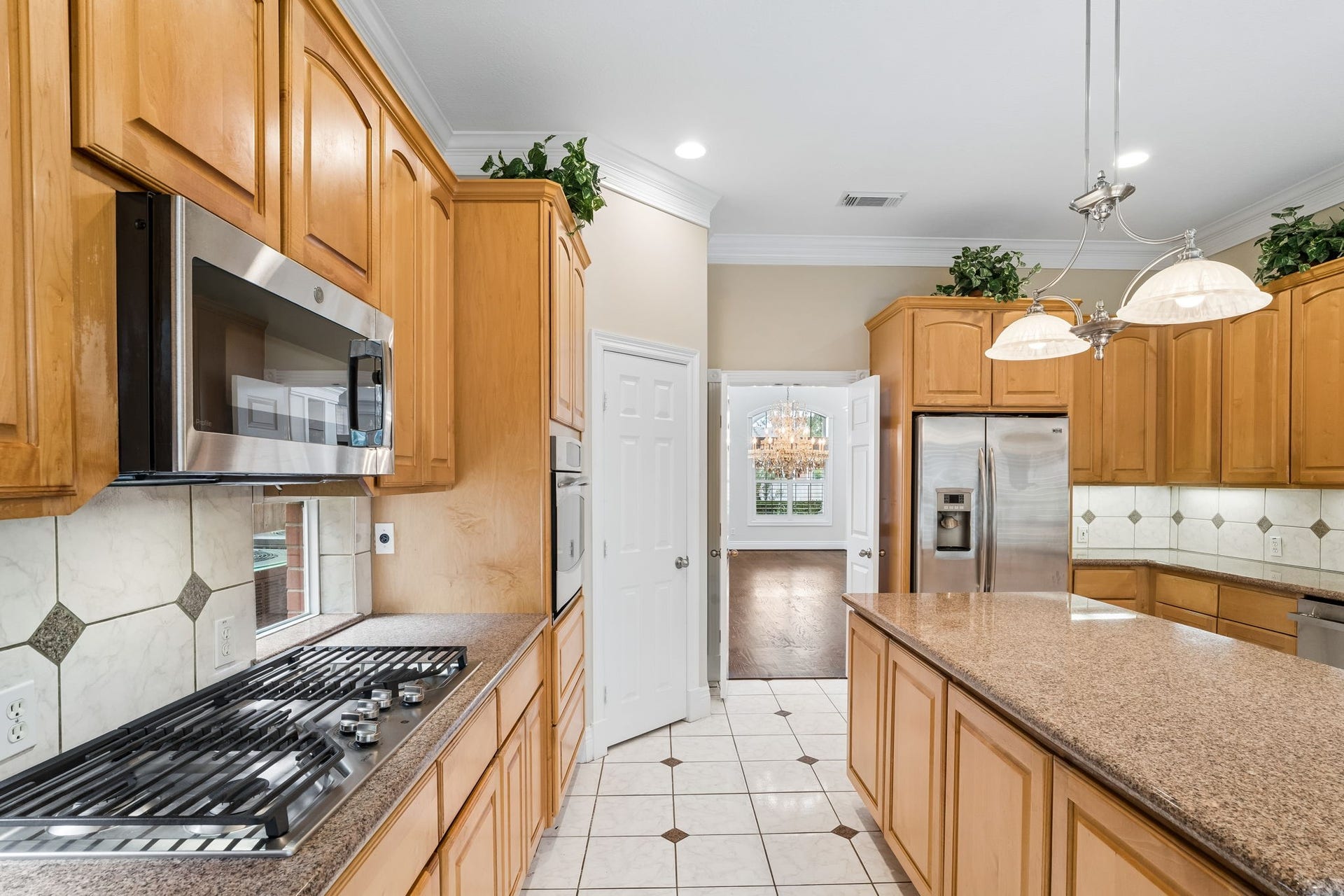 Spacious kitchen with elegant tile flooring, featuring a large central island, warm wood cabinetry, and stainless steel appliances. Arched doorways lead to a cozy living room with a fireplace, creating a seamless flow for entertaining.