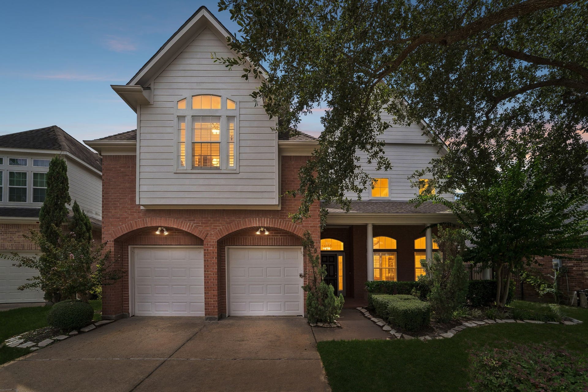 Charming two-story home with a brick and siding exterior, with inviting front porch surrounded by landscaped greenery.