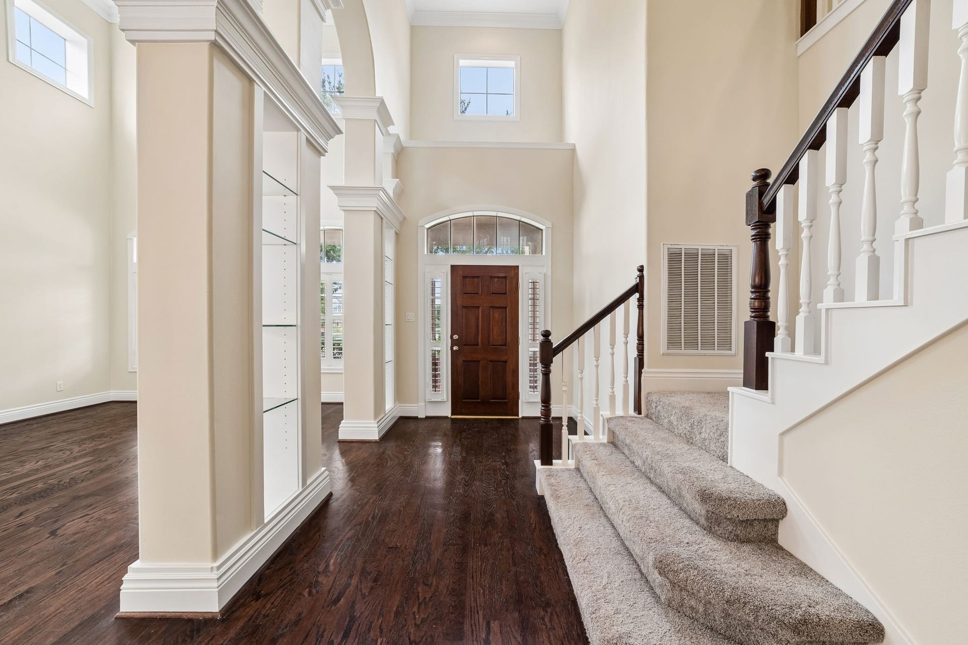Elegant foyer with a grand staircase, rich wood flooring, and abundant natural light from French doors, offering a welcoming and spacious entryway.