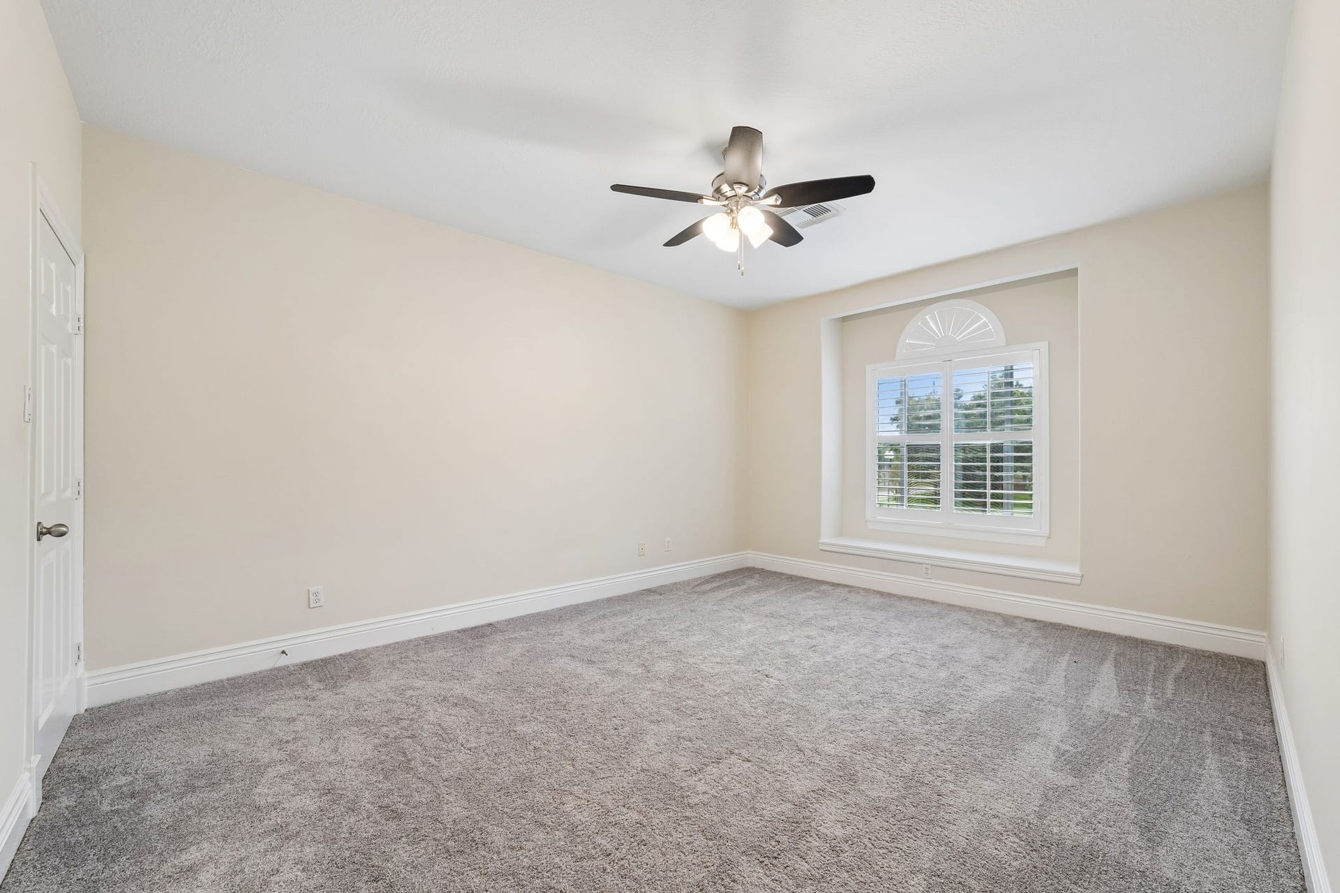 Spacious second-floor bedroom#2 featuring plush carpeting, a ceiling fan, and a large window with plantation shutters that brings in abundant natural light.