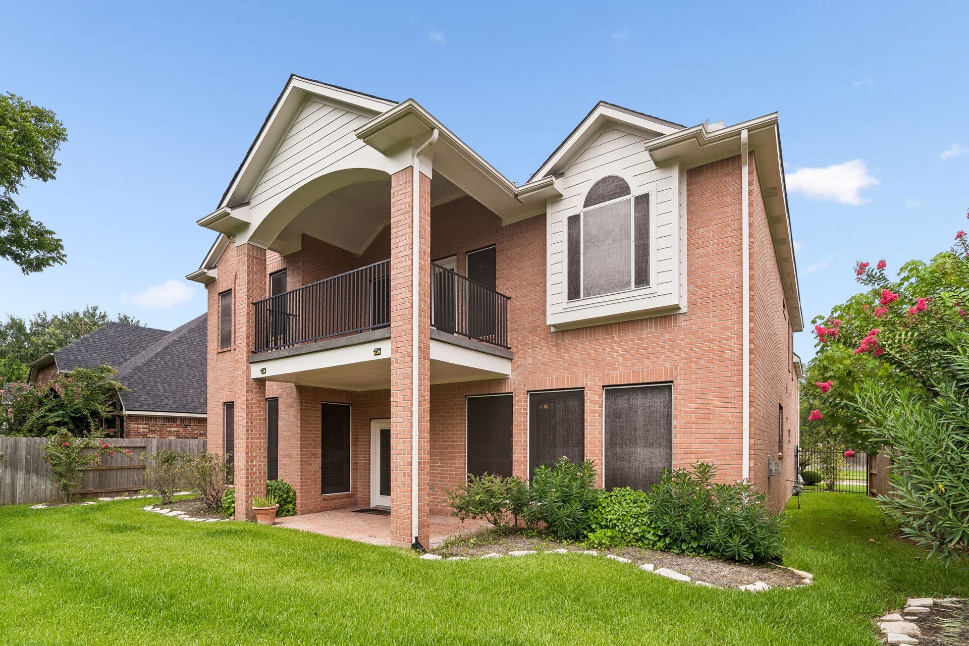 Elegant two-story brick home with a covered balcony and a well-maintained lawn, offering a spacious and inviting outdoor space.