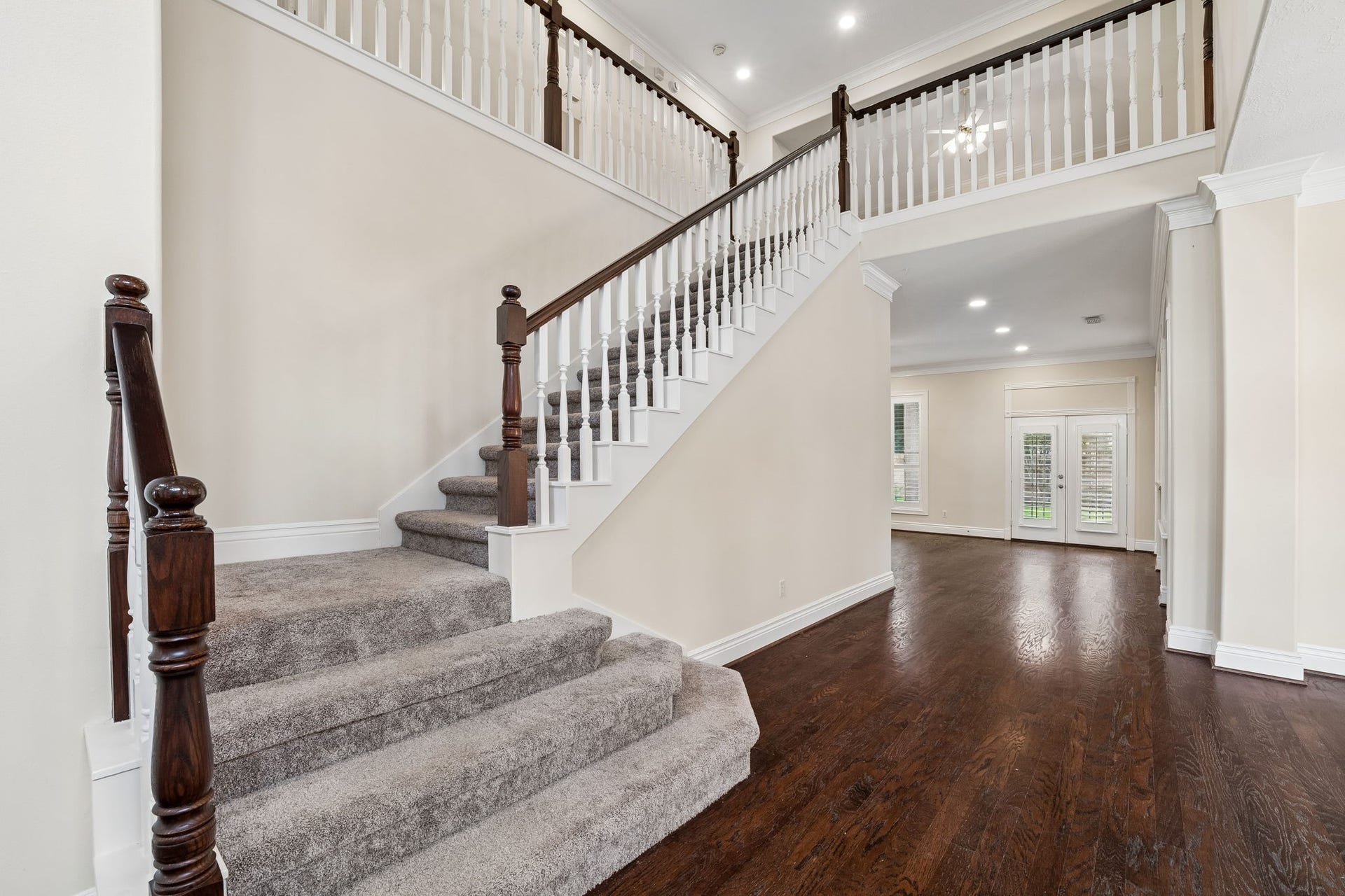 Step into elegance with this grand entryway featuring rich hardwood floors, a stunning staircase, and a glimpse of a luxurious chandelier in the open living area.