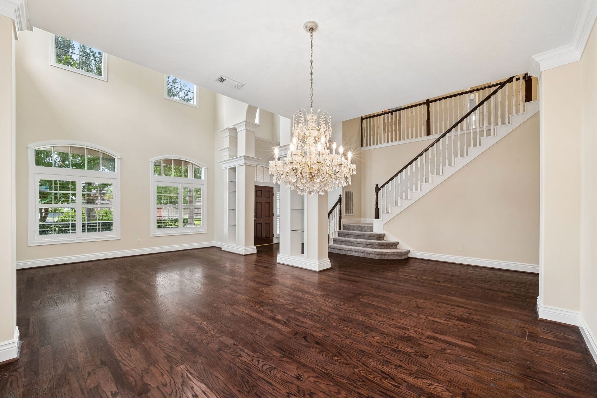Elegant living space with high ceilings, large arched windows, and a stunning chandelier, offering abundant natural light and rich hardwood floors.