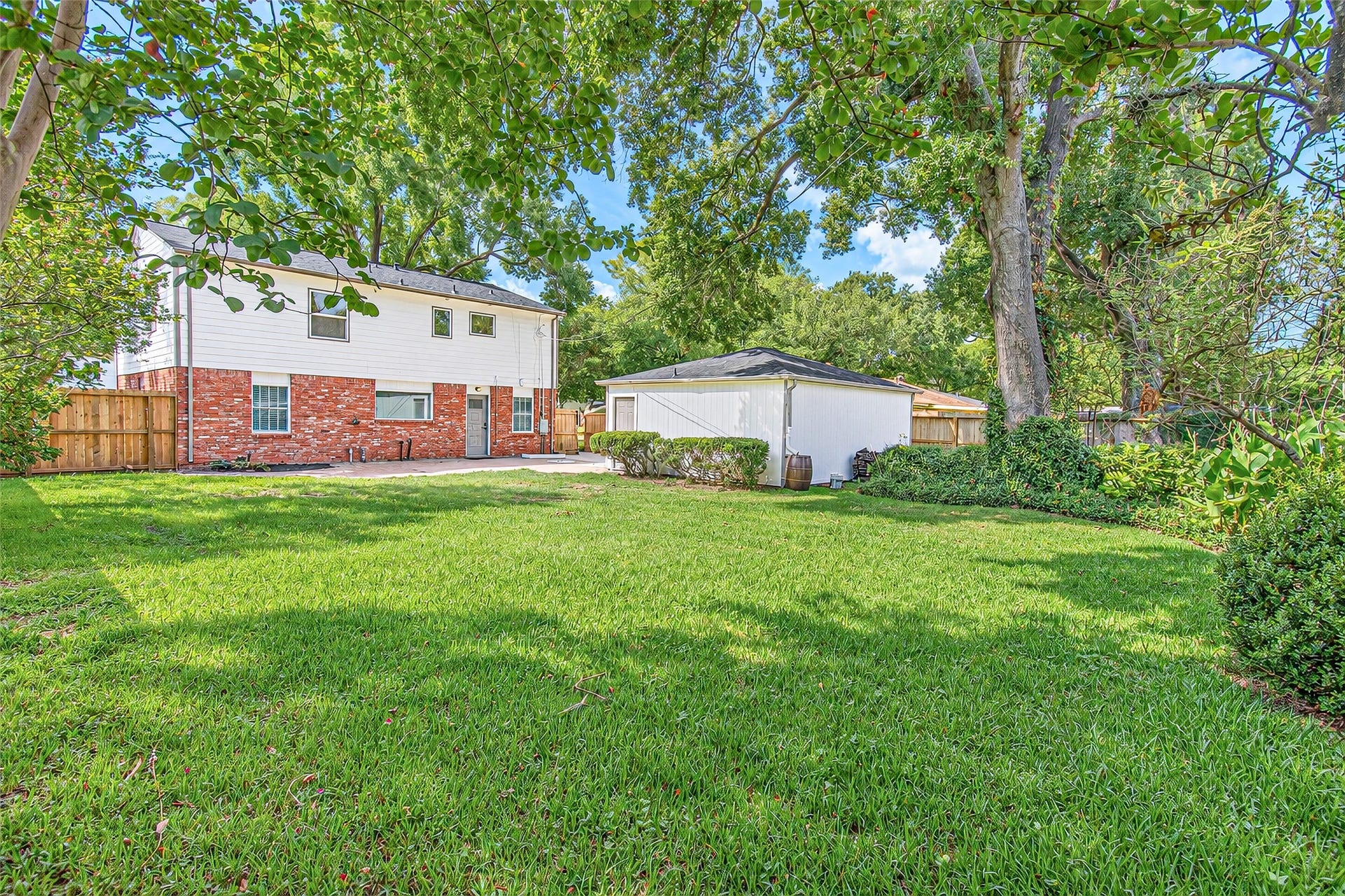 10610 Overbrook Lane, Houston, TX 77042 Spacious backyard with lush green lawn, charming brick and siding exterior, and a detached garage, all surrounded by mature trees for added privacy.