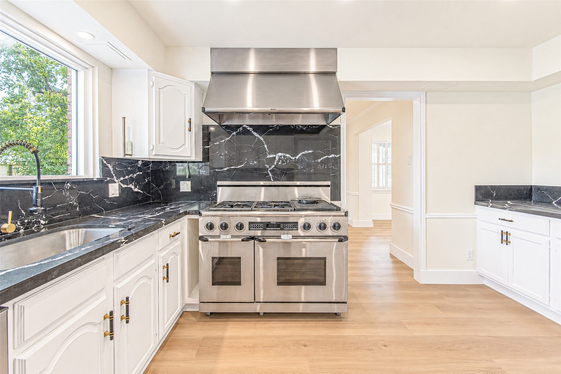 10610 Overbrook Lane, Houston, TX 77042 Modern kitchen featuring a sleek stainless steel stove, elegant black quartz countertops, and white cabinetry with stylish brass handles.