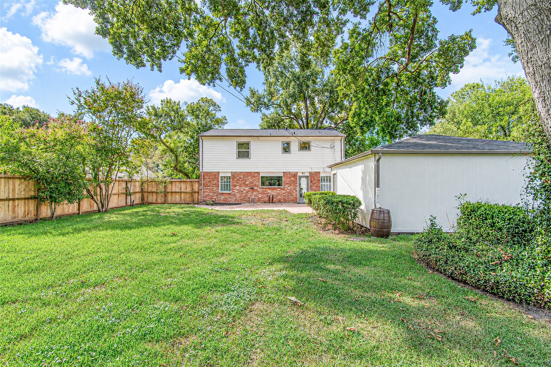 10610 Overbrook Lane, Houston, TX 77042 Spacious backyard with lush green grass, mature trees, and a privacy fence, complemented by a charming two-story home featuring a mix of brick and siding.