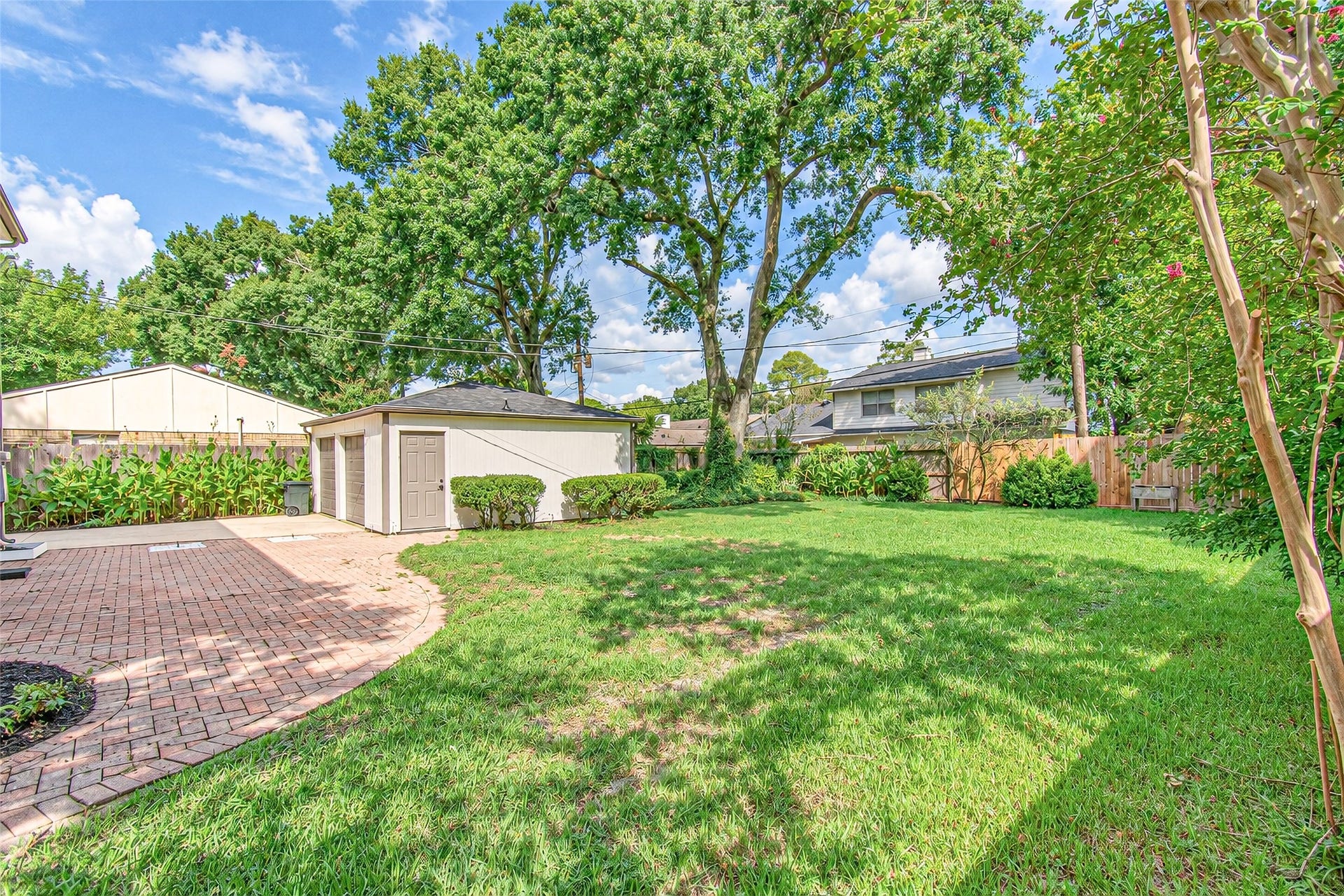 10610 Overbrook Lane, Houston, TX 77042 Spacious backyard with lush green lawn, mature trees, and a charming brick patio, perfect for outdoor gatherings.
