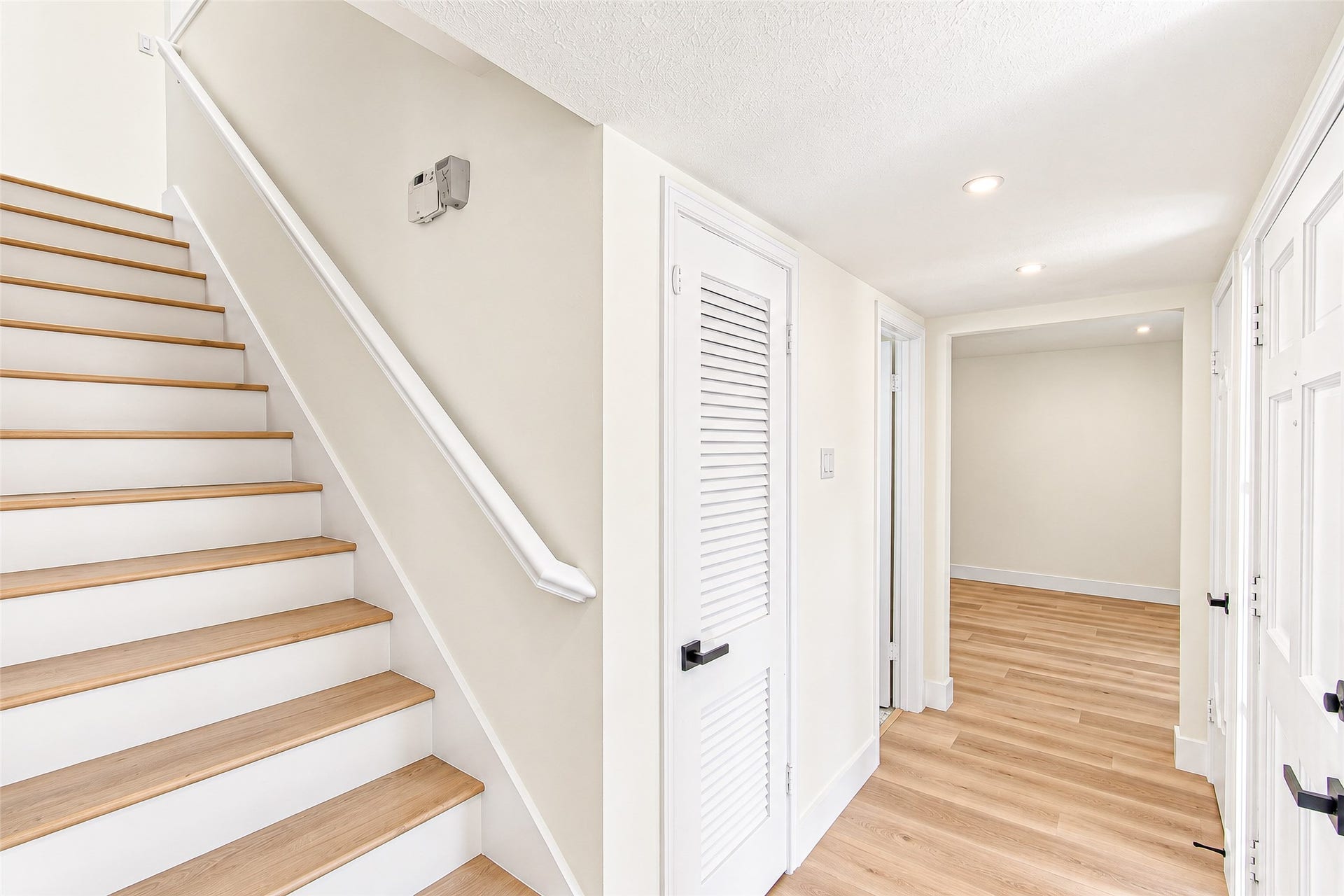 10610 Overbrook Lane, Houston, TX 77042 Bright and inviting hallway featuring sleek vinylflooring, crisp white walls, and modern recessed lighting leading to multiple rooms and an elegant staircase.