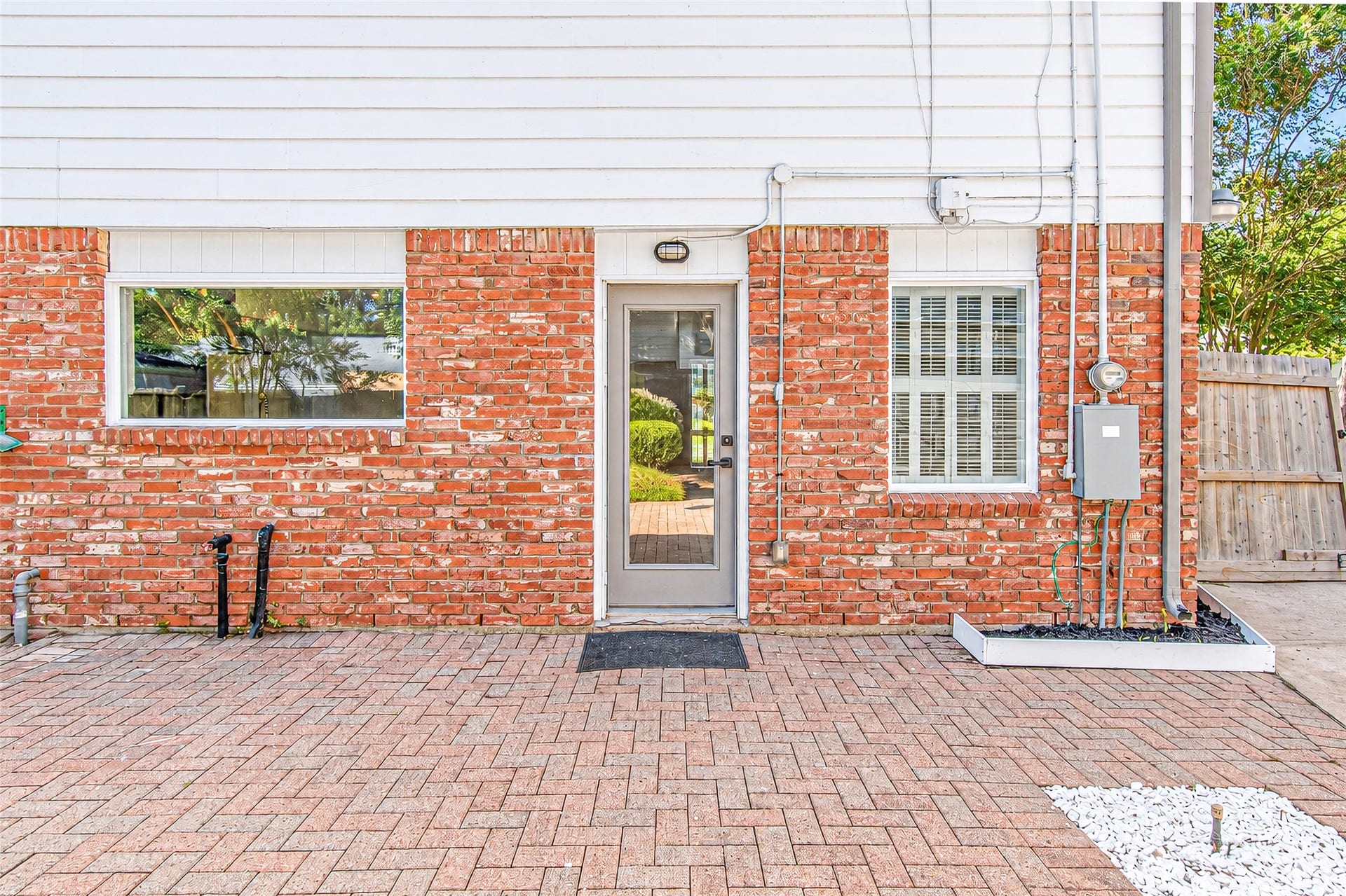 10610 Overbrook Lane, Houston, TX 77042 Charming brick exterior with a modern glass door, flanked by large windows for ample natural light, opens to a spacious paved patio perfect for outdoor living.