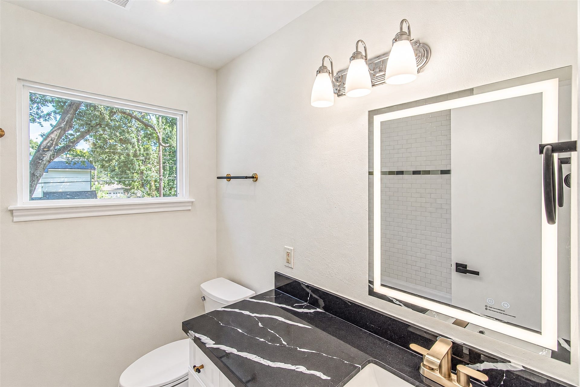 10610 Overbrook Lane, Houston, TX 77042 The second bath boasts a sleek design with a modern black countertop, elegant gold fixtures, and a bright window, creating a refreshing and stylish space.