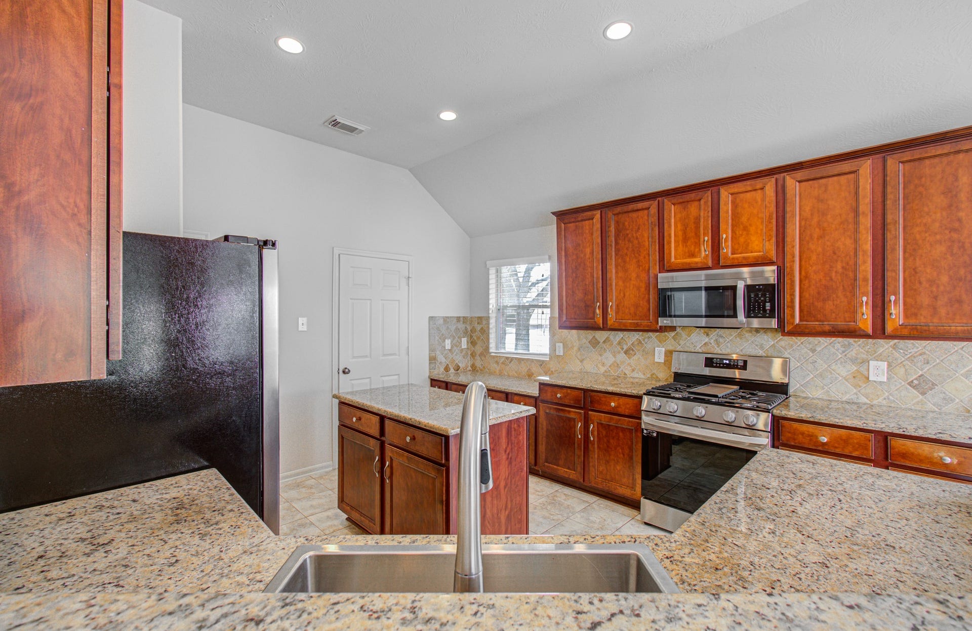 12808 Brook Arbor Court, Pearland, TX 77584 Elegant kitchen featuring rich wood cabinetry, granite countertops, and modern stainless steel appliances, complemented by a stylish tile backsplash.