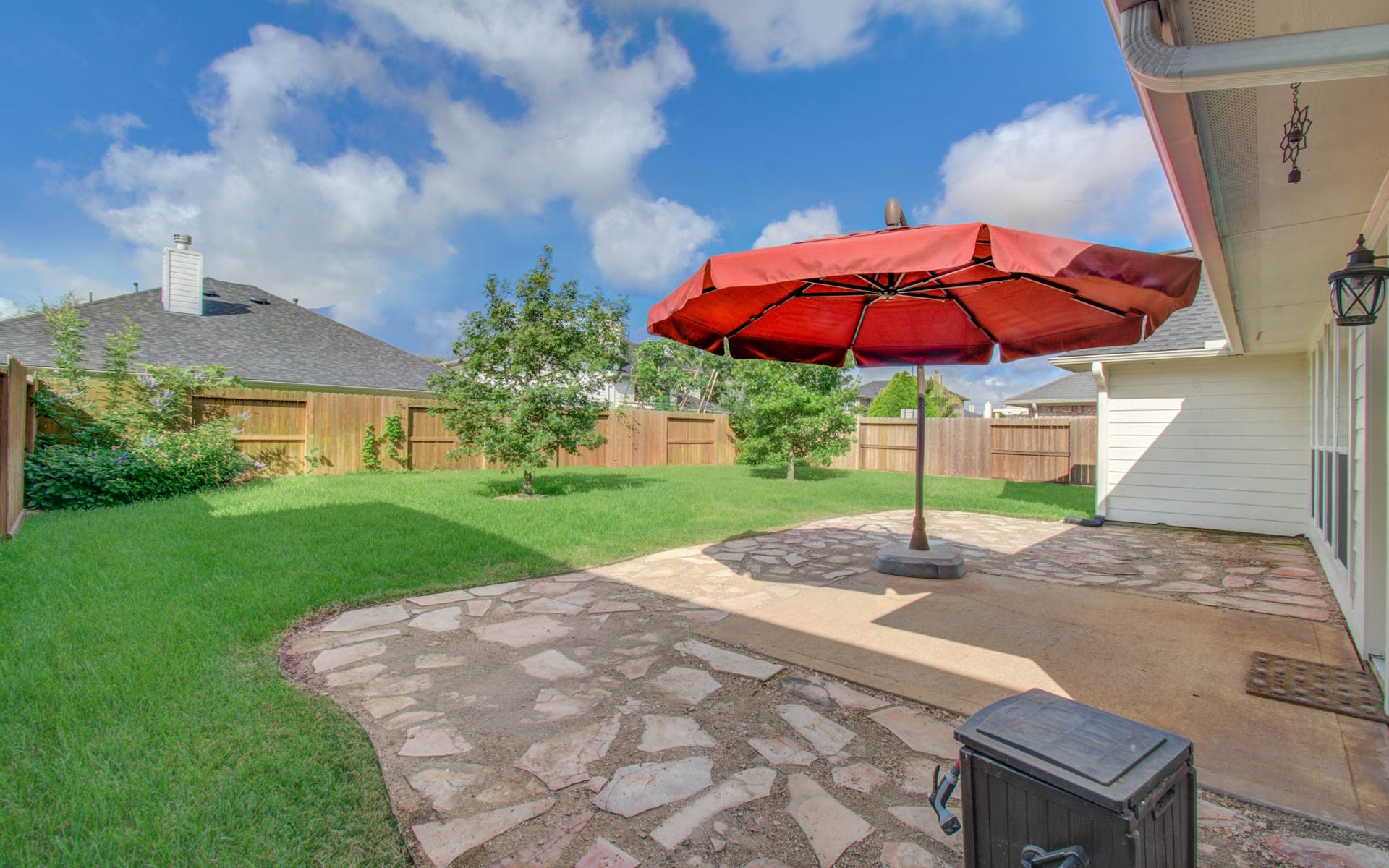 12808 Brook Arbor Court, Pearland, TX 77584 Spacious backyard features a charming stone patio with a large umbrella, perfect for outdoor gatherings and relaxation.