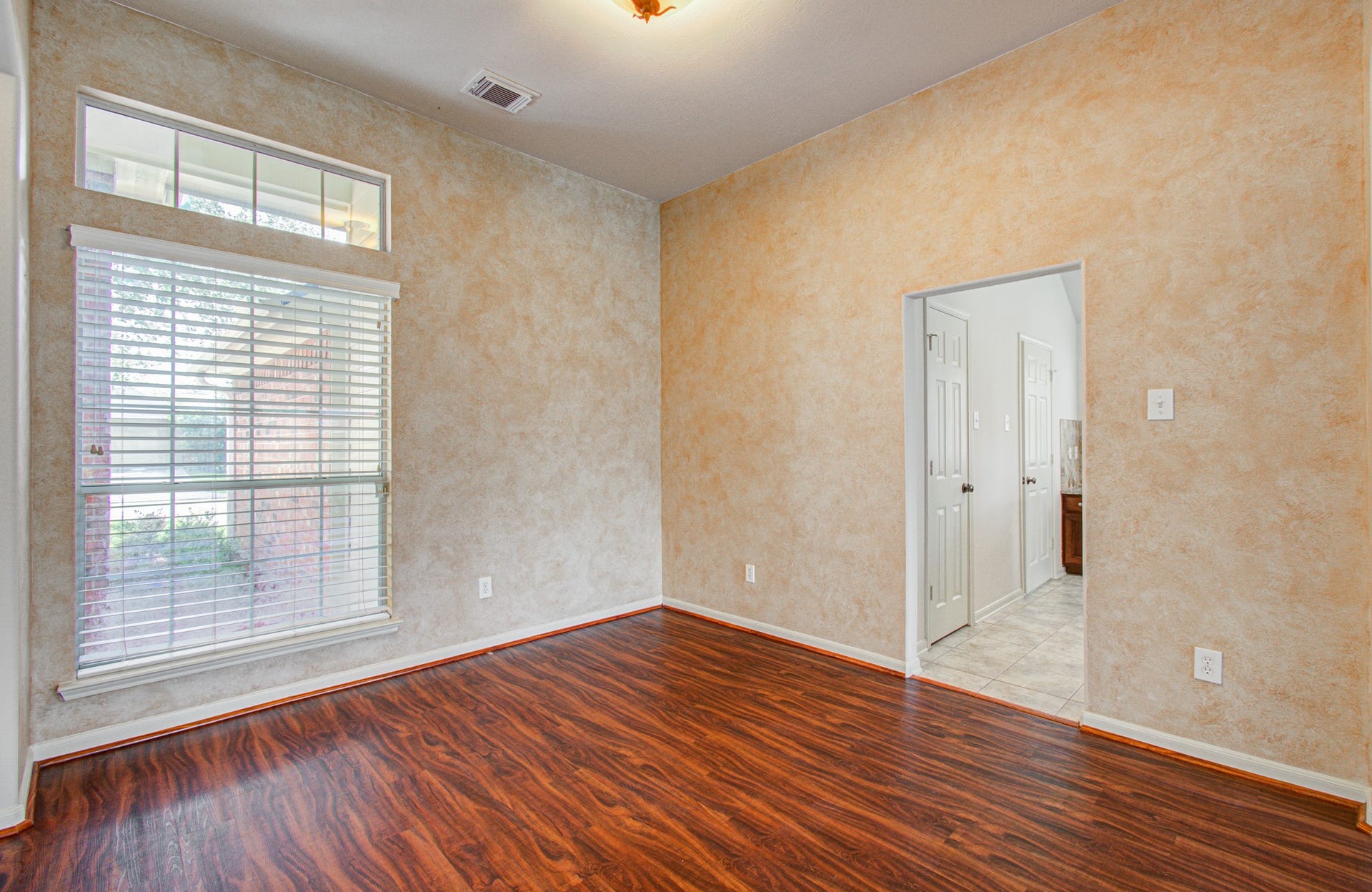 12808 Brook Arbor Court, Pearland, TX 77584 Inviting open space with rich wood flooring, a large window for natural light, and a warm, textured wall finish, leading to the kitchen