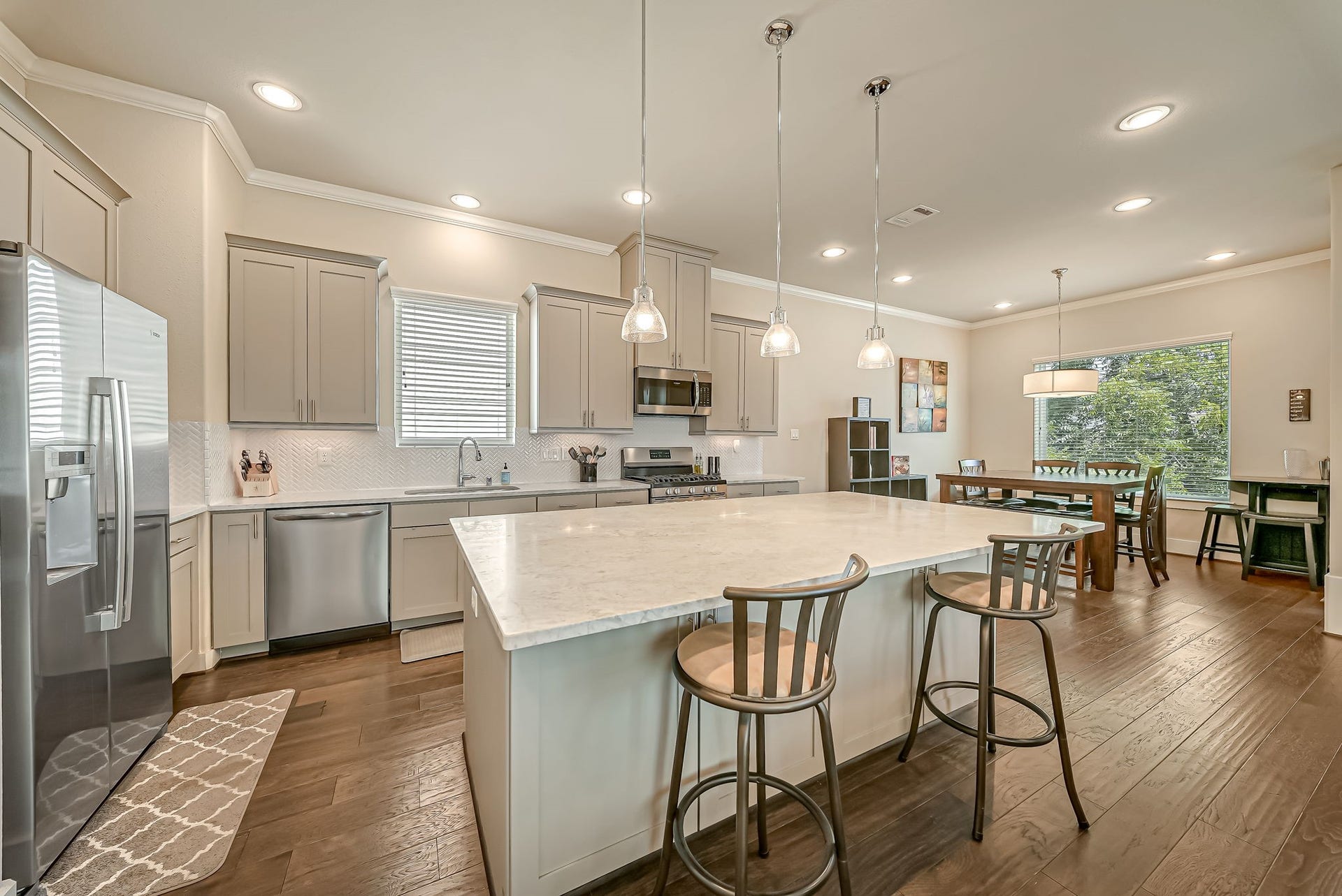 5916 Petty Street, #A, Houston, TX 77007 Chef-inspired kitchen showcasing an oversized marble island, stainless steel appliances, soft-close cabinetry, wine chiller, and stylish herringbone backsplash.