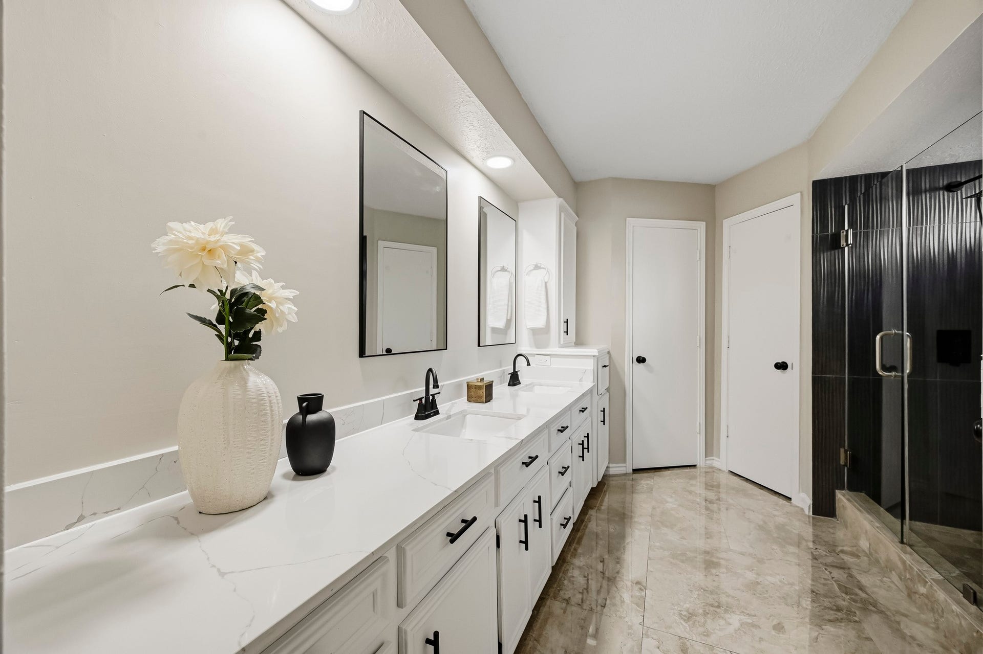 6714 Brittany Park Lane, Houston, TX 77066 Elegant bathroom featuring a double vanity with sleek black fixtures, large mirrors, and a spacious glass-enclosed shower, all set against sophisticated tile flooring.