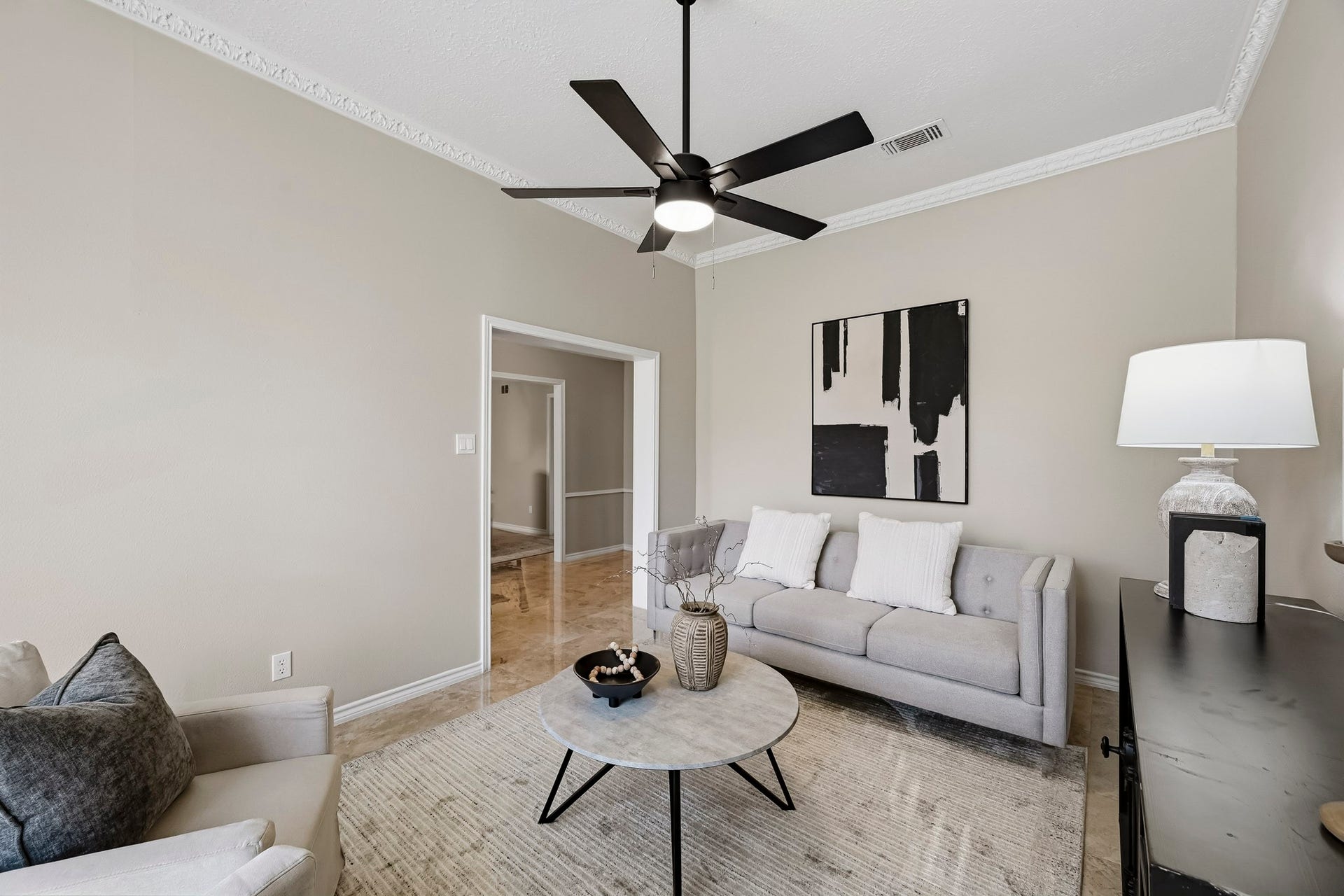 6714 Brittany Park Lane, Houston, TX 77066 Charming living room with modern ceiling fan, neutral walls, and elegant crown molding. Cozy seating area includes a stylish sofa and armchair, complemented by contemporary decor and soft lighting.
