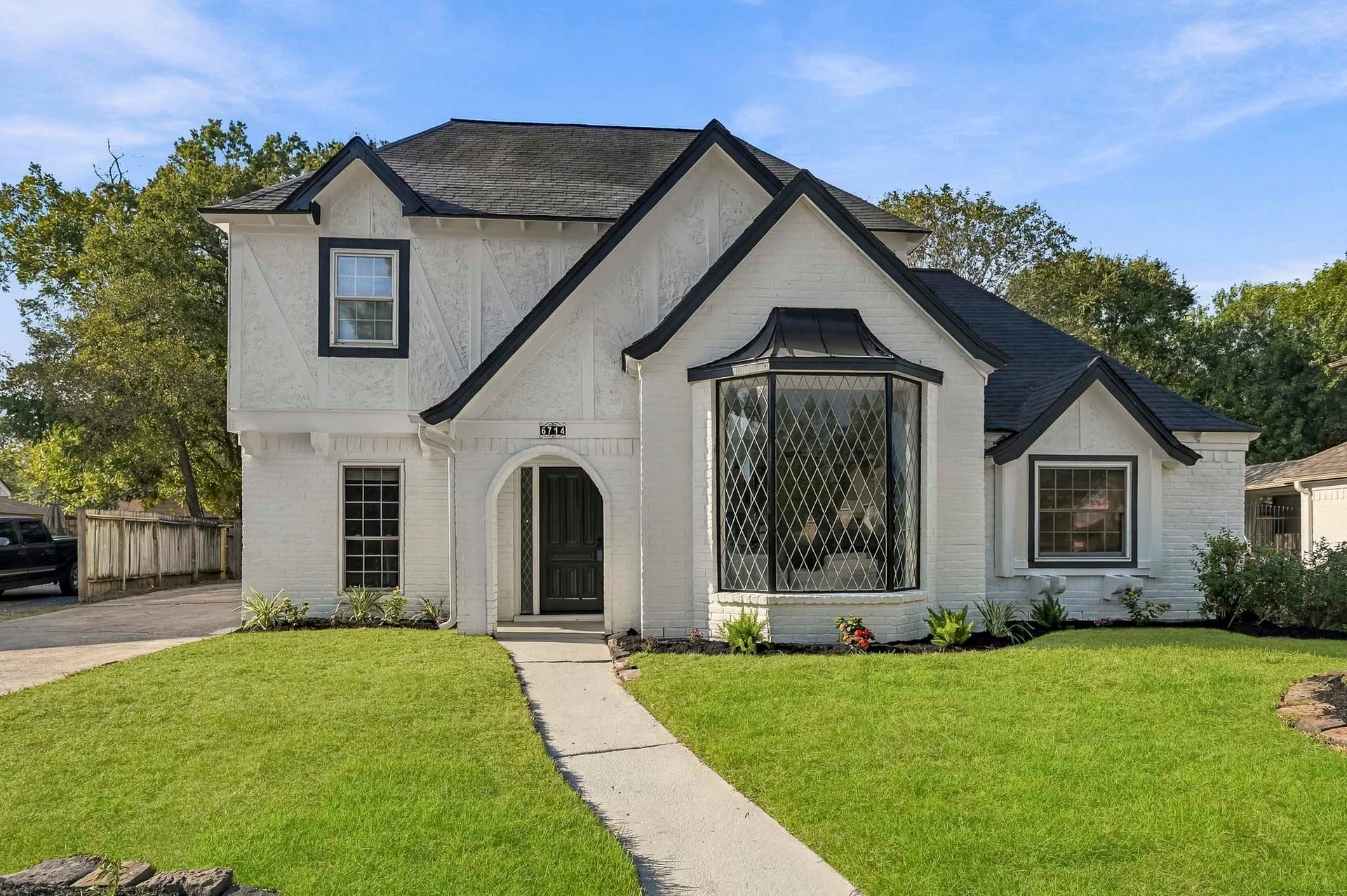 6714 Brittany Park Lane, Houston, TX 77066 Charming two-story home with elegant Tudor-style architecture, featuring a distinctive bay window and inviting arched entryway, surrounded by a lush, manicured lawn.