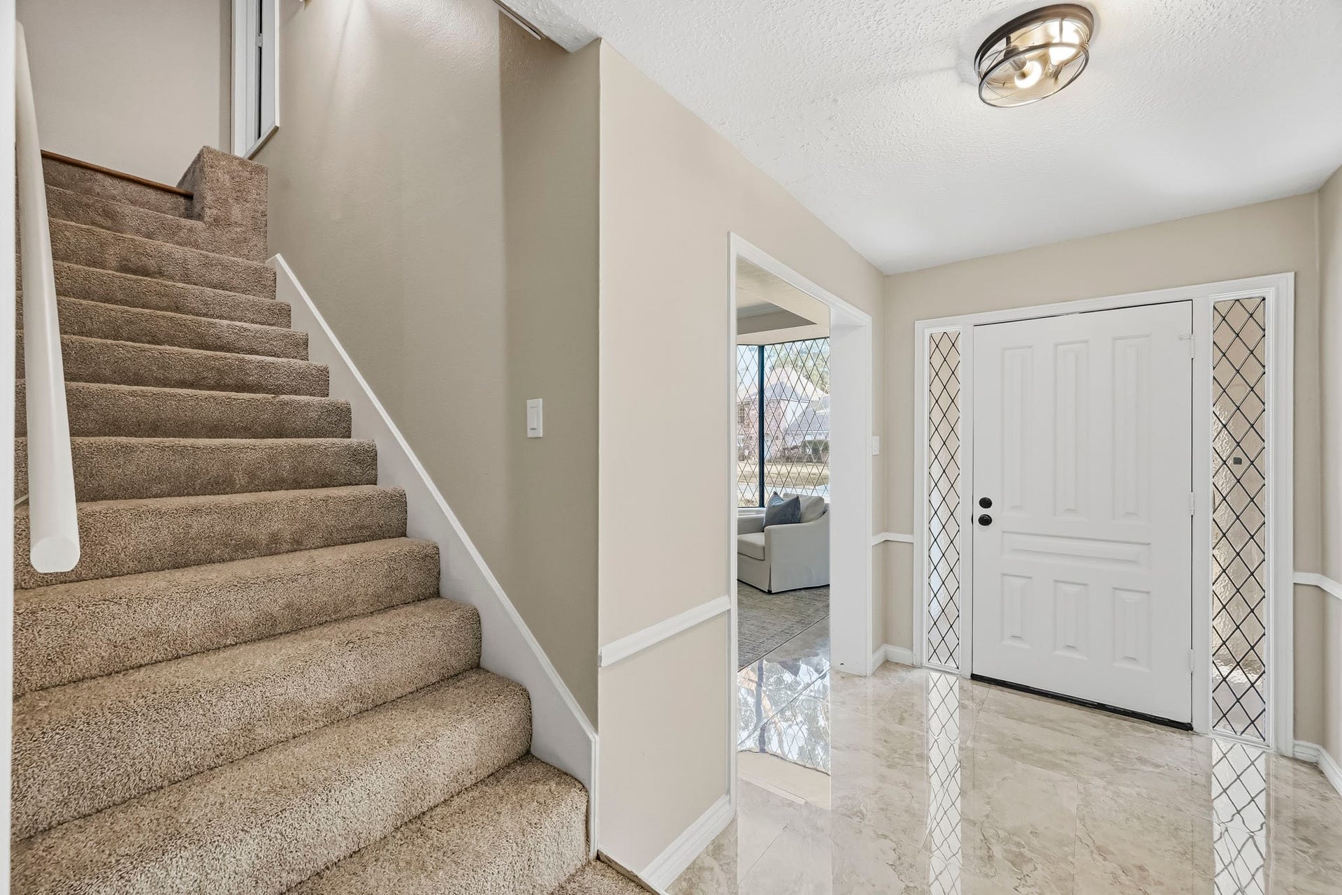 6714 Brittany Park Lane, Houston, TX 77066 Inviting entryway featuring elegant marble flooring, a classic white door with decorative side panels, and plush carpeted stairs leading to the second floor.
